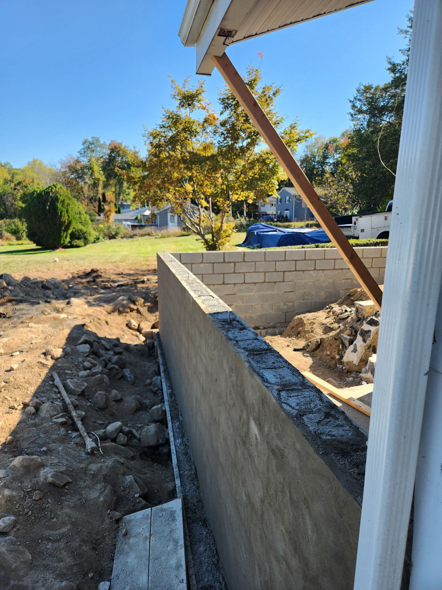 Backyard construction site with a new concrete retaining wall and dirt excavation under a patio roof
