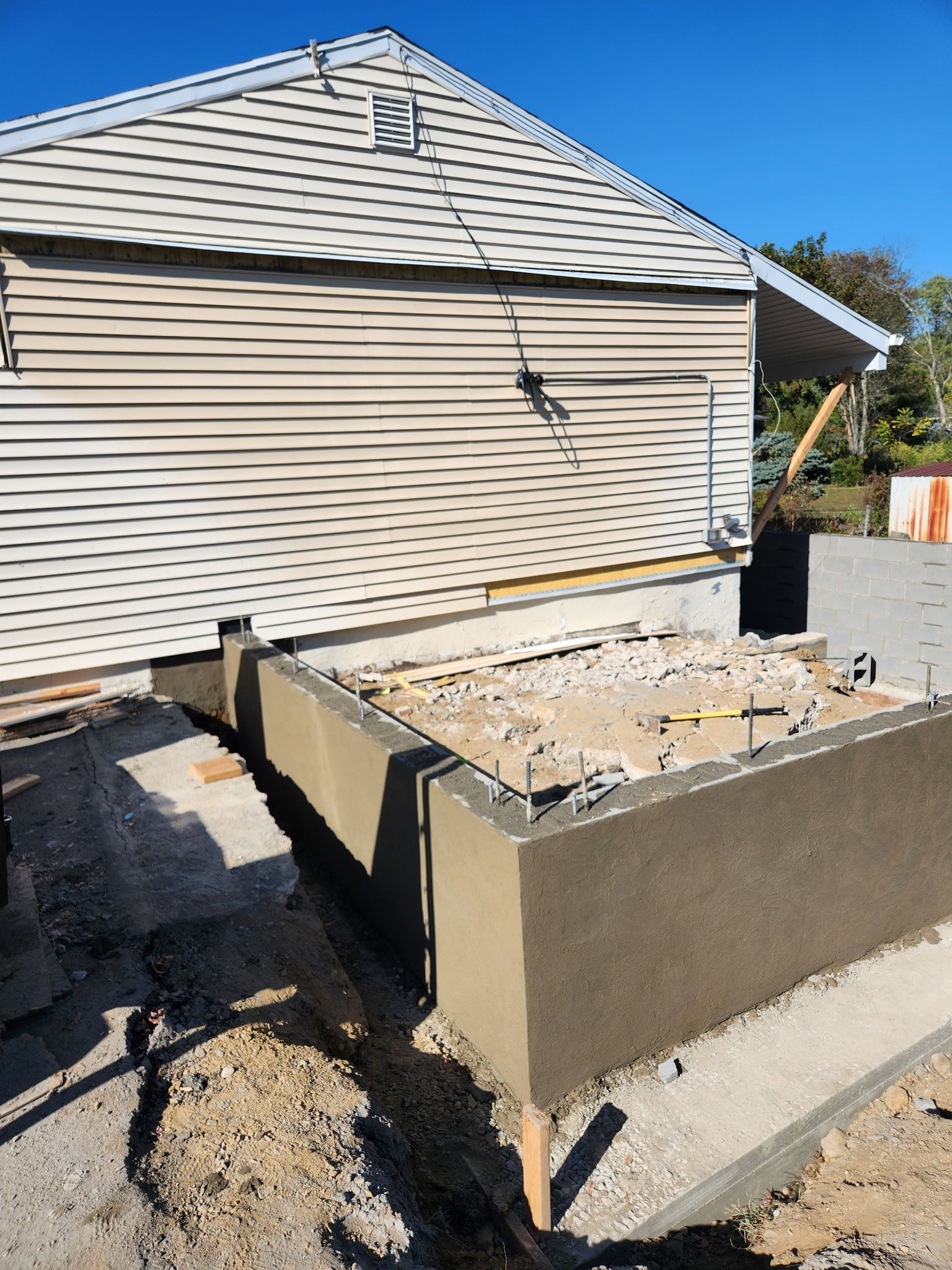 Backyard concrete planter bed beside a beige house with newly built retaining walls and rubble inside
