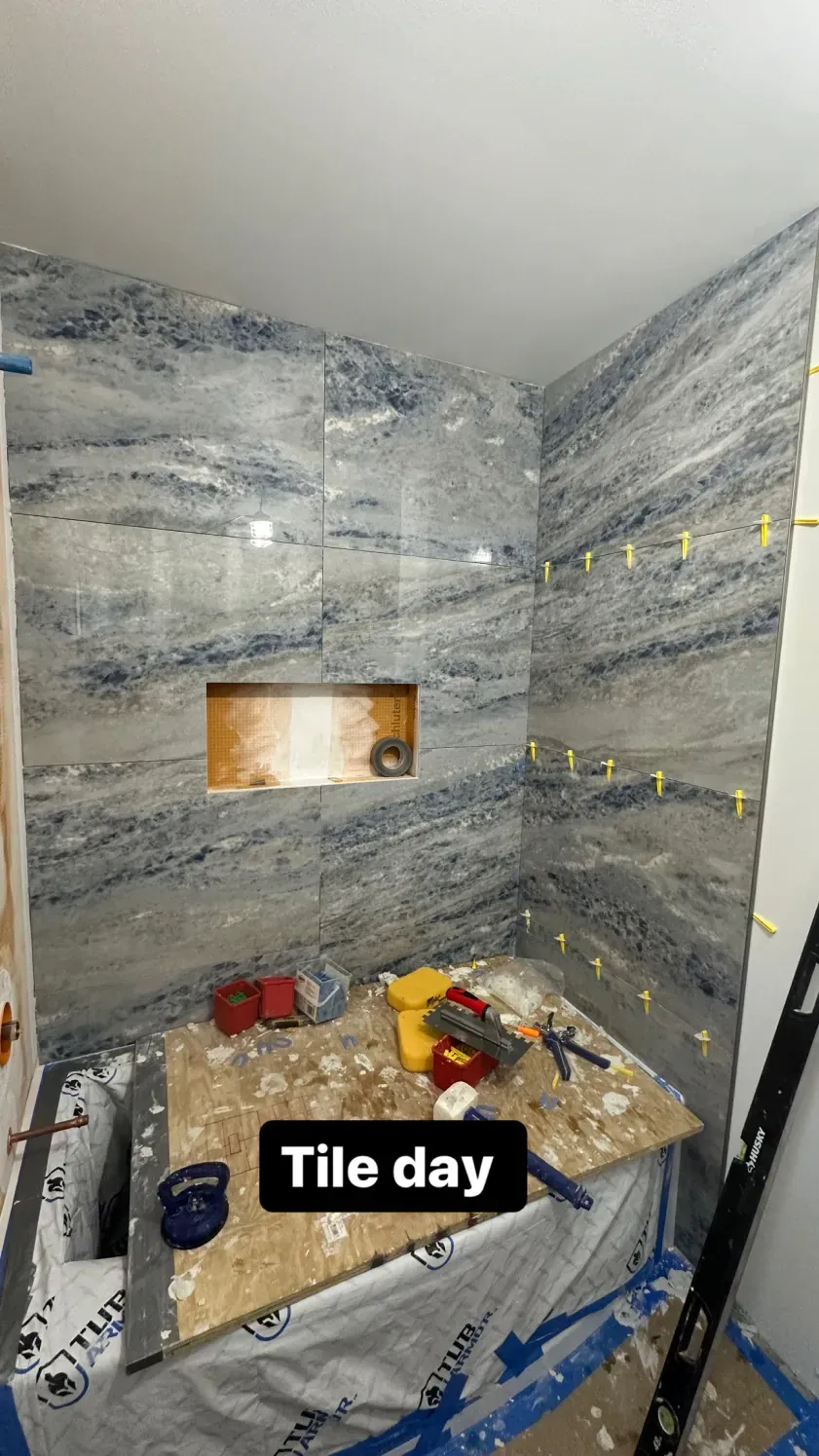 Bathroom with blue-veined tile in shower during renovation. Tools and materials on a board.