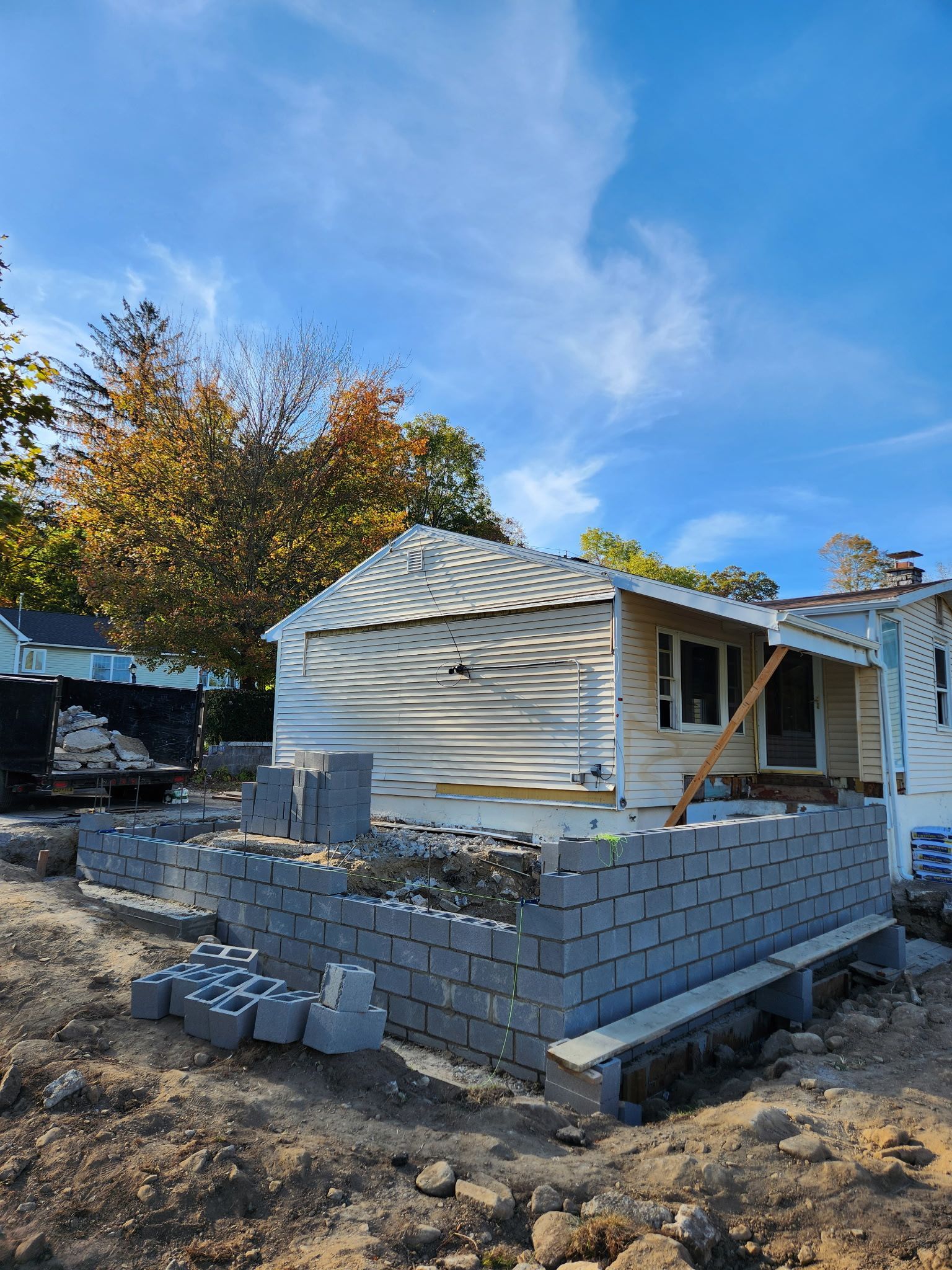 Partially built white house with cinder block foundation and debris in a wooded yard