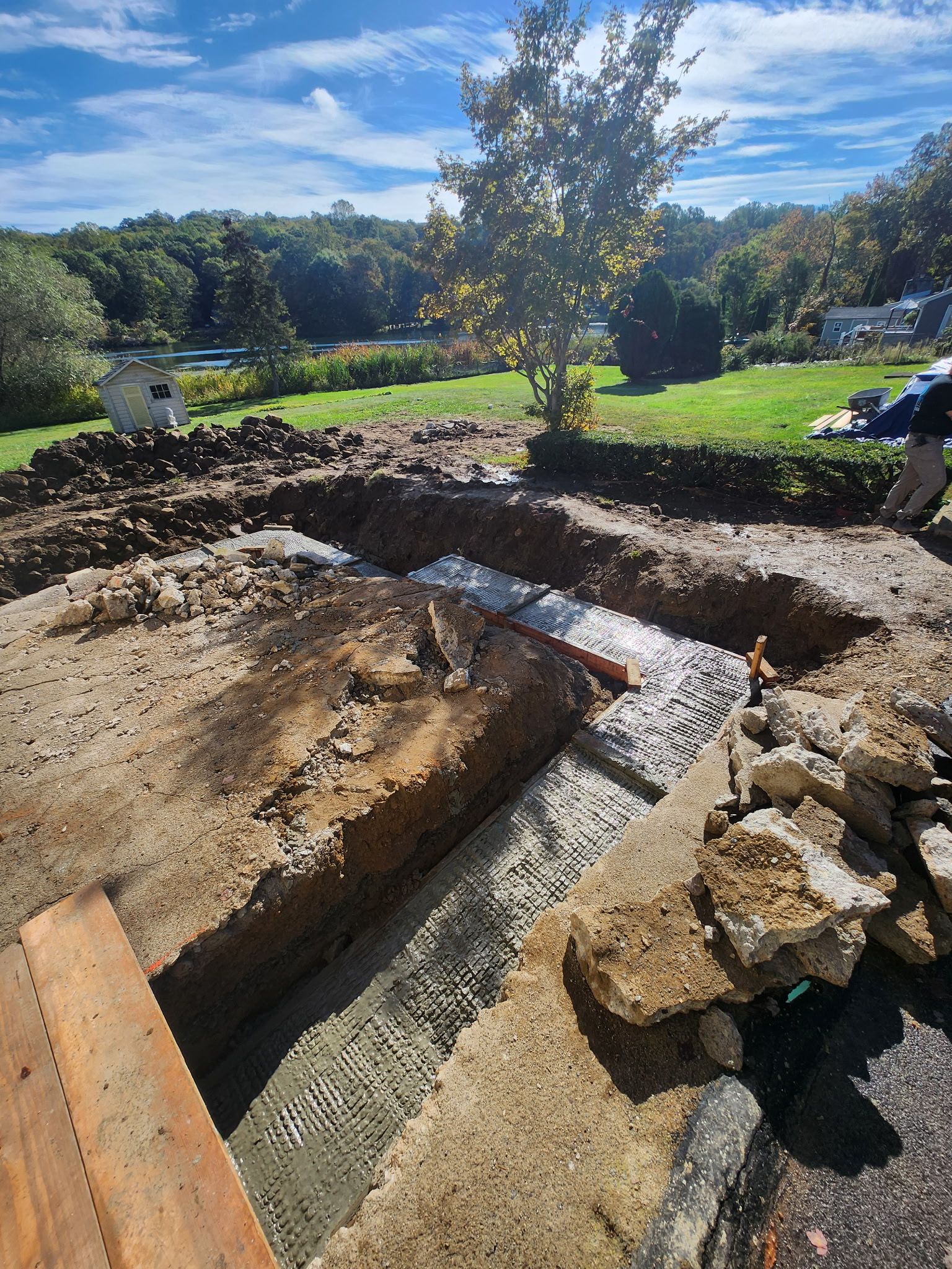 Fresh concrete trench and excavation site in a sunny grassy yard with a tree in the center.