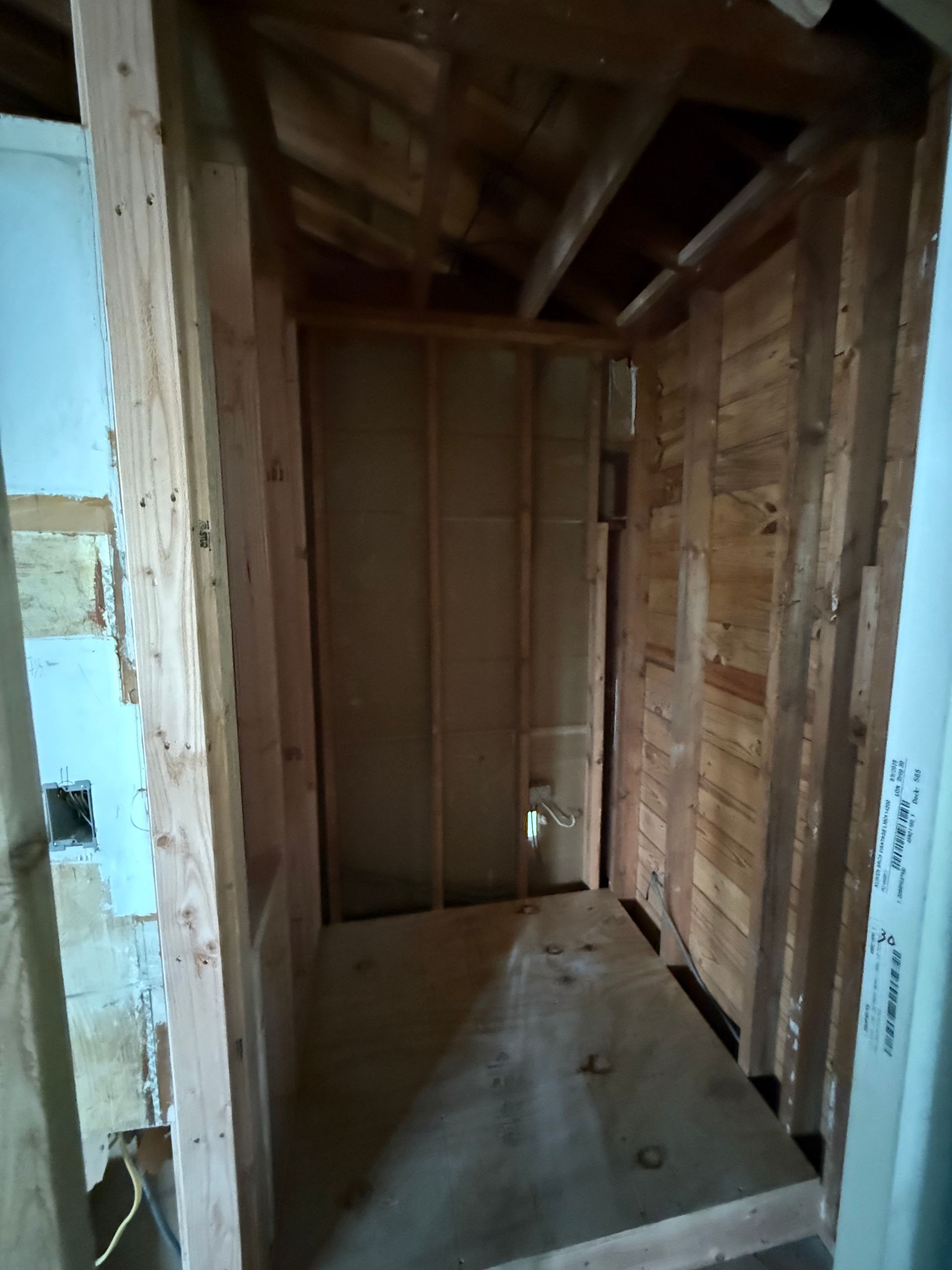 Narrow unfinished hallway with exposed wood framing and a concrete floor inside a house under construction