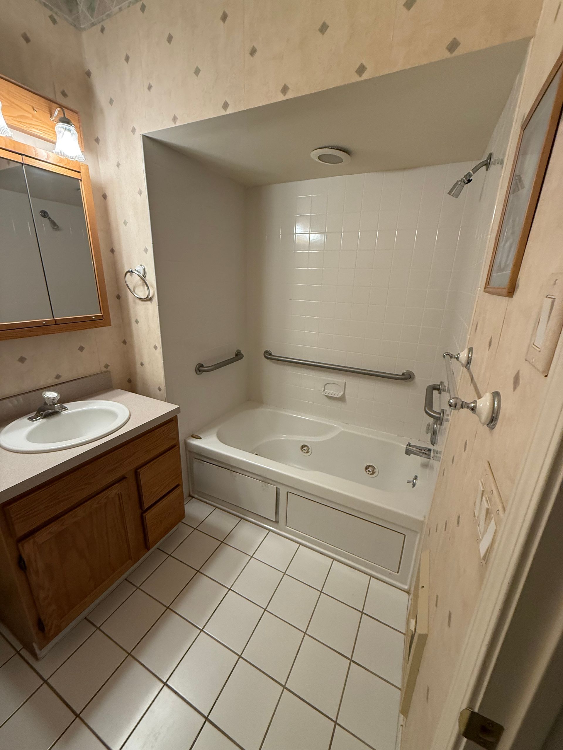 Small bathroom with white tiled walk-in tub shower, sink vanity, and tiled floor.