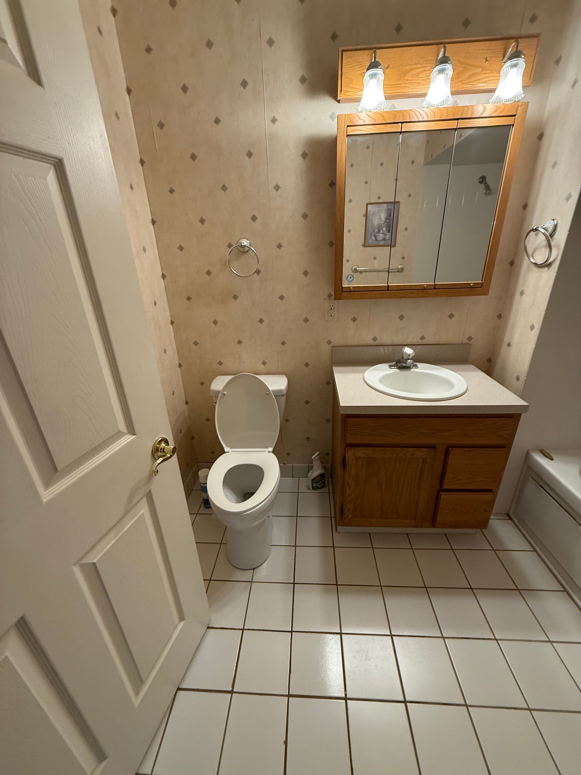 Small bathroom with open toilet, wood vanity, mirror, and tiled floor.