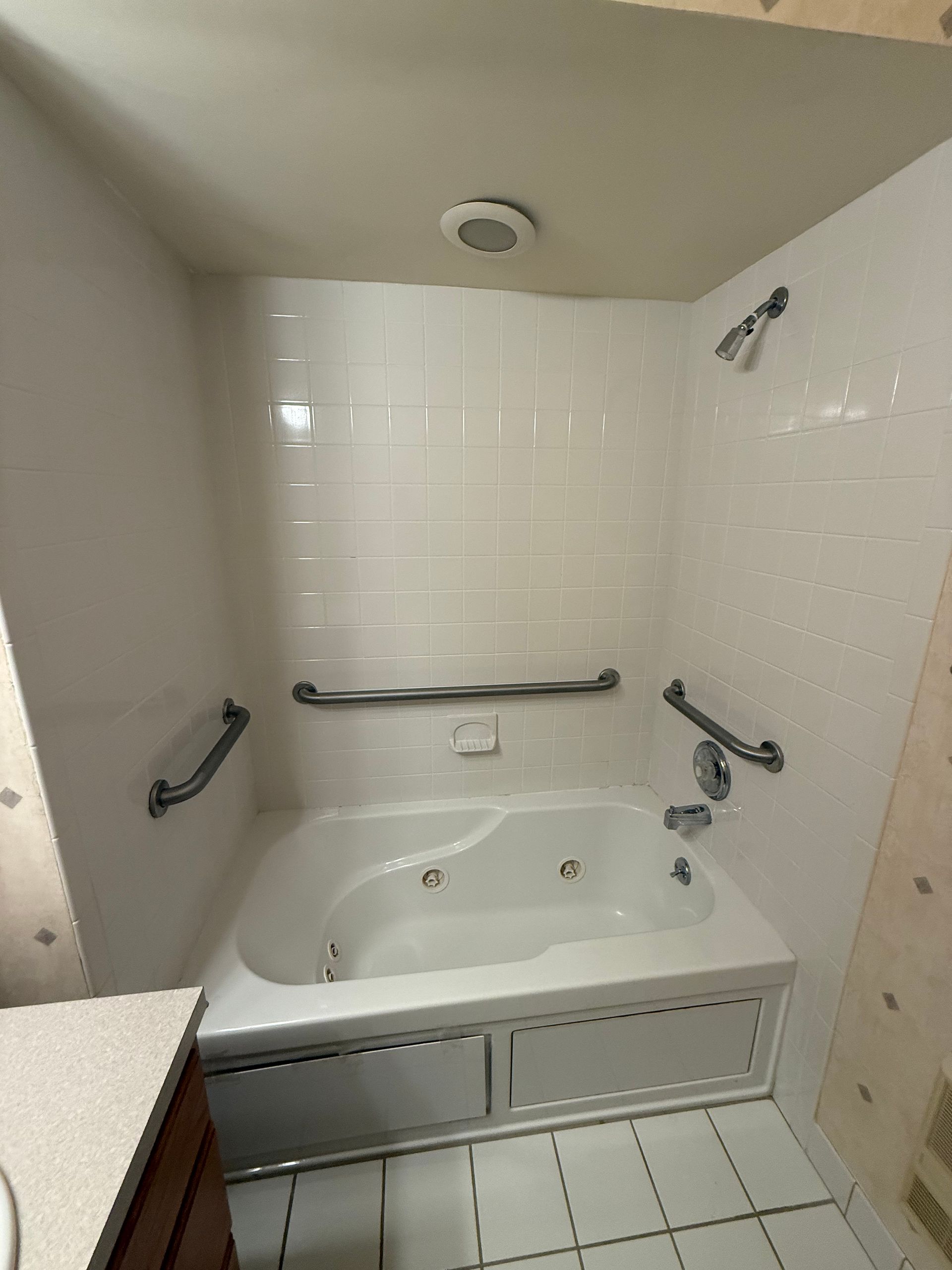 Accessible white bathtub with grab bars, handheld shower, and tiled surround in a bathroom