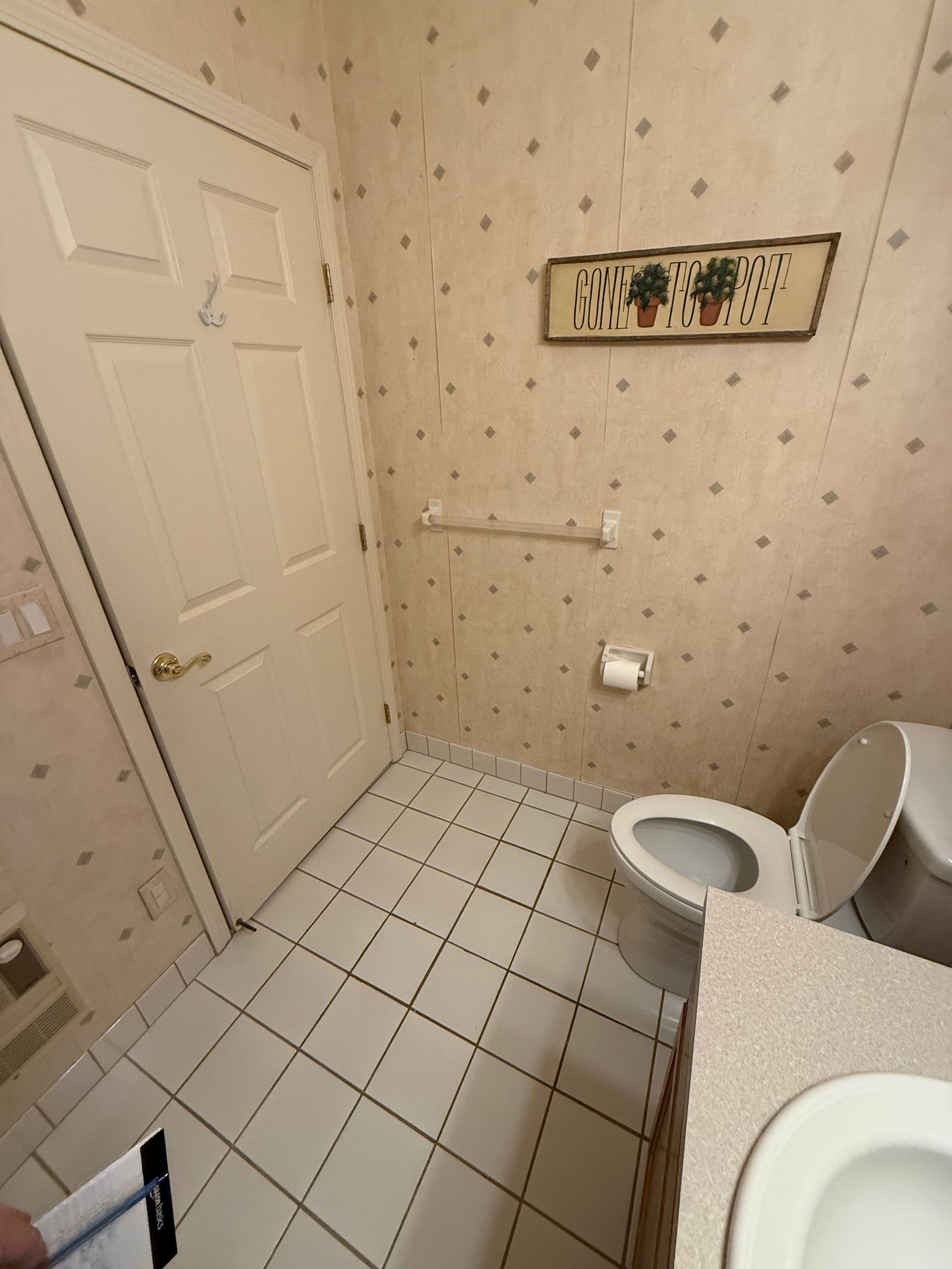 Small beige bathroom with a toilet, tiled floor, and towel rack beside a white door.
