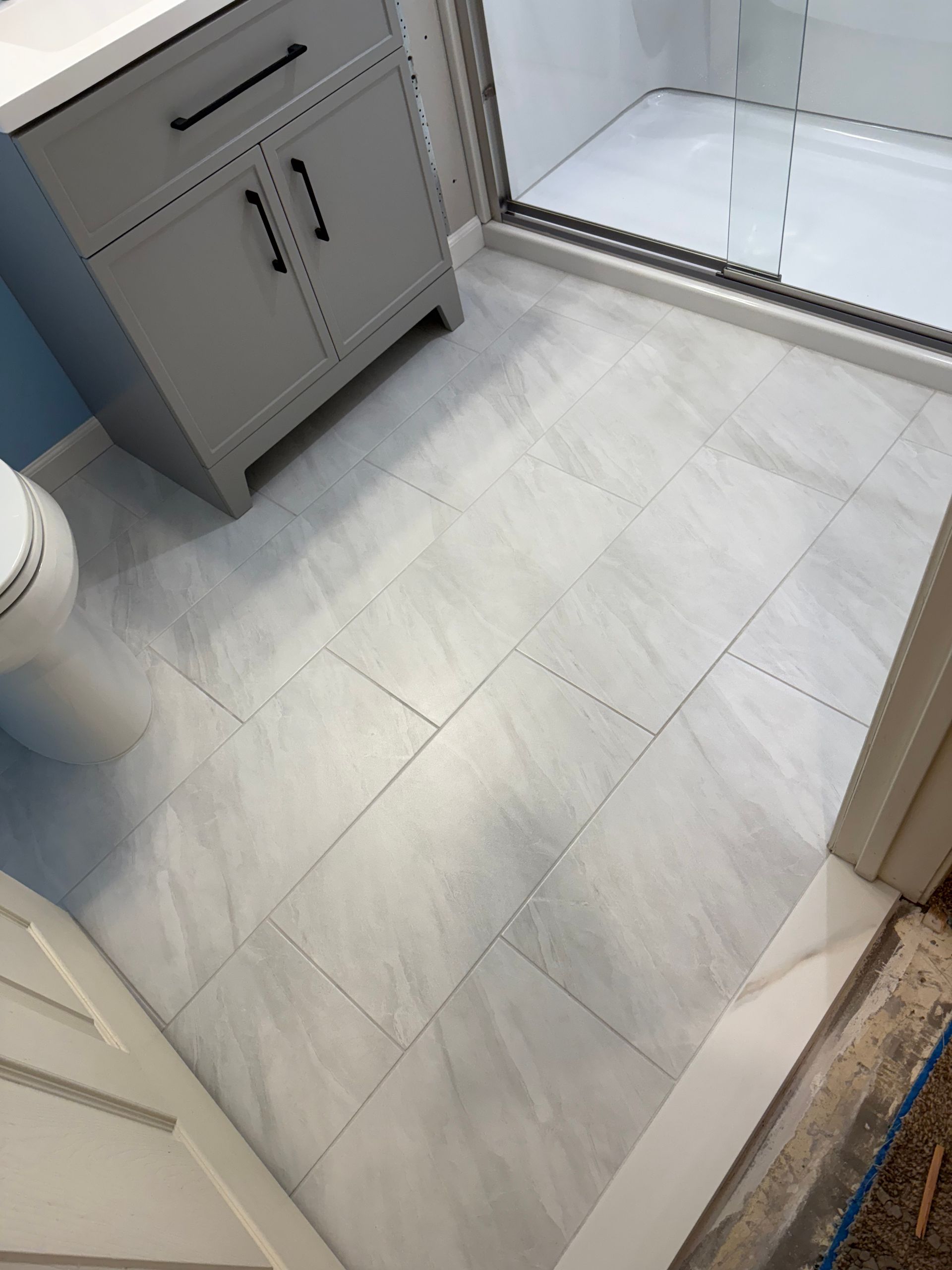Light gray tiled bathroom floor beside a cabinet and glass shower door