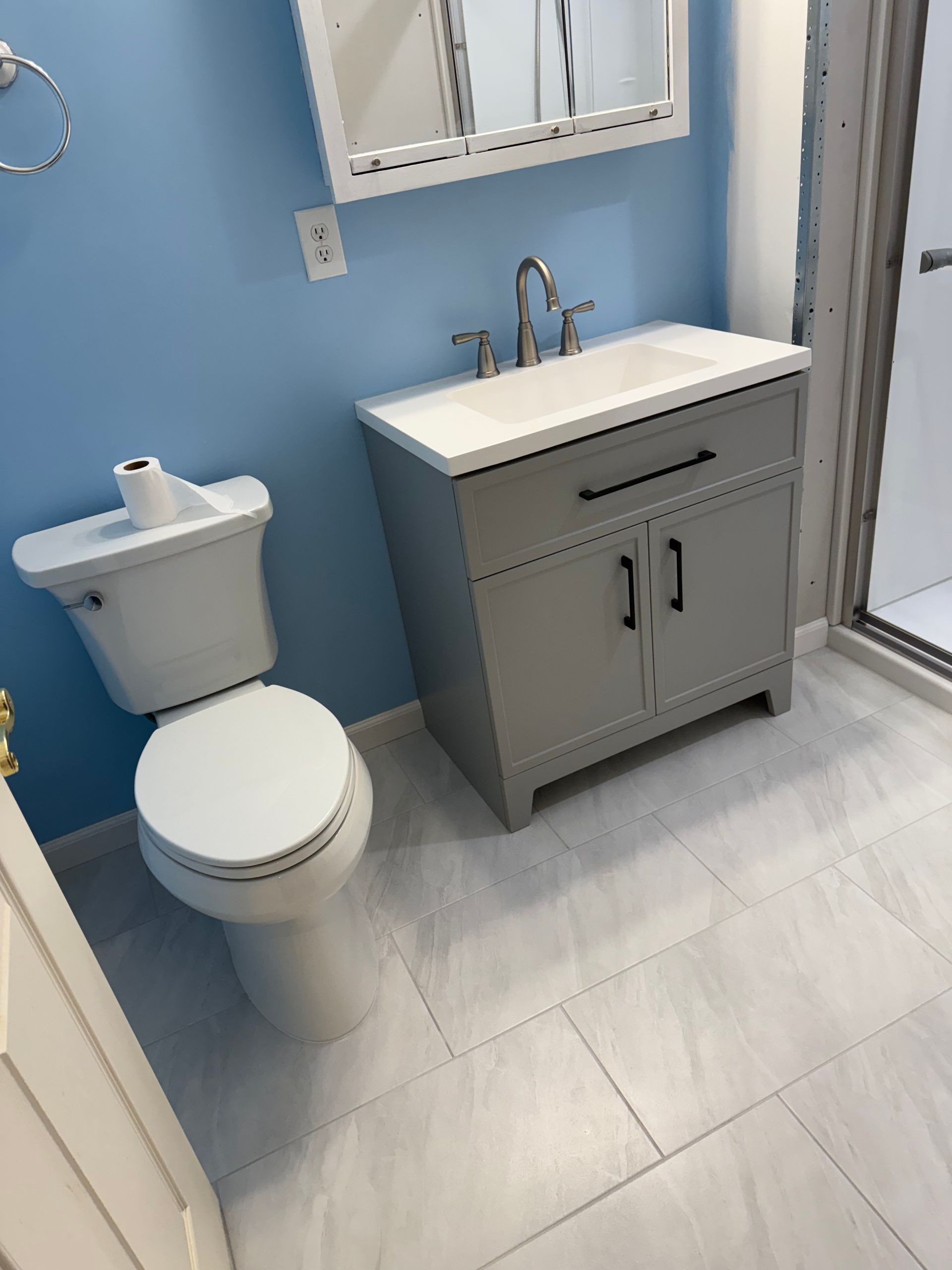 Small blue bathroom with toilet, sink vanity, mirror, and shower stall.