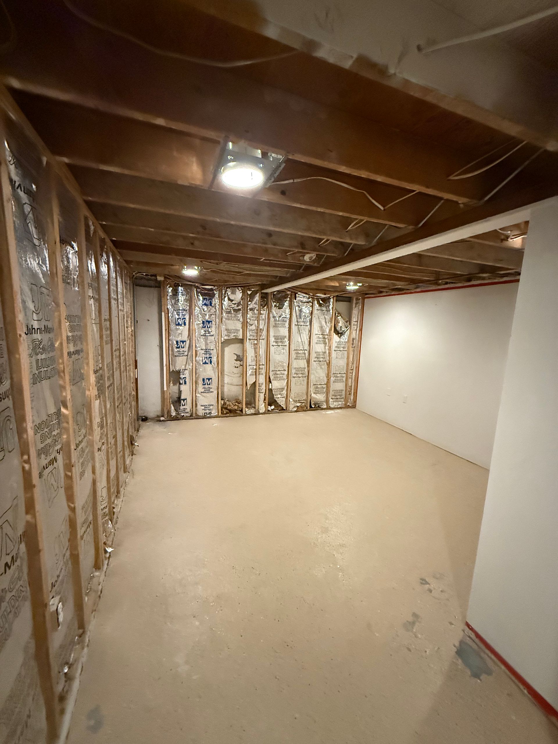Unfinished basement with exposed insulation, open ceiling joists, and bare concrete floor