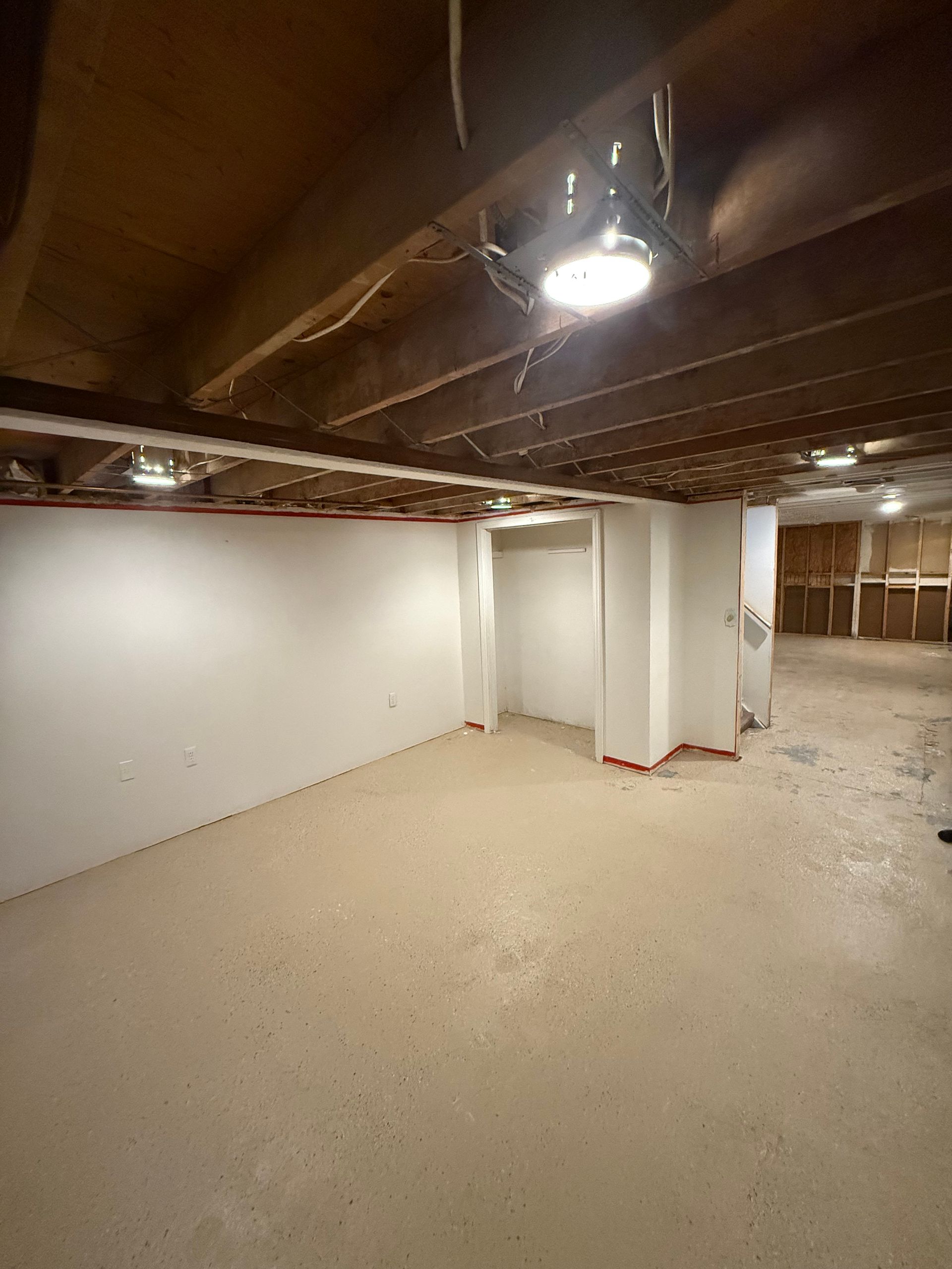 Empty unfinished basement with exposed beams, white walls, support columns, and bare concrete floor.