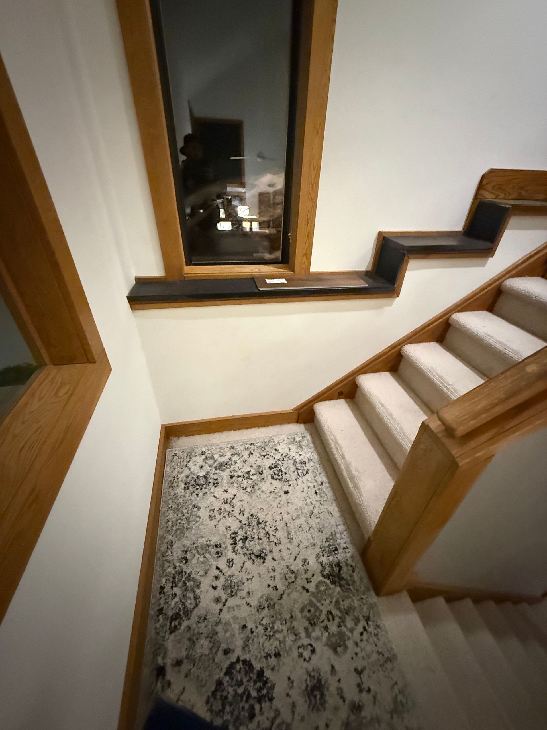 Interior staircase with wood railings, a patterned runner, and a window overlooking the outside at night.