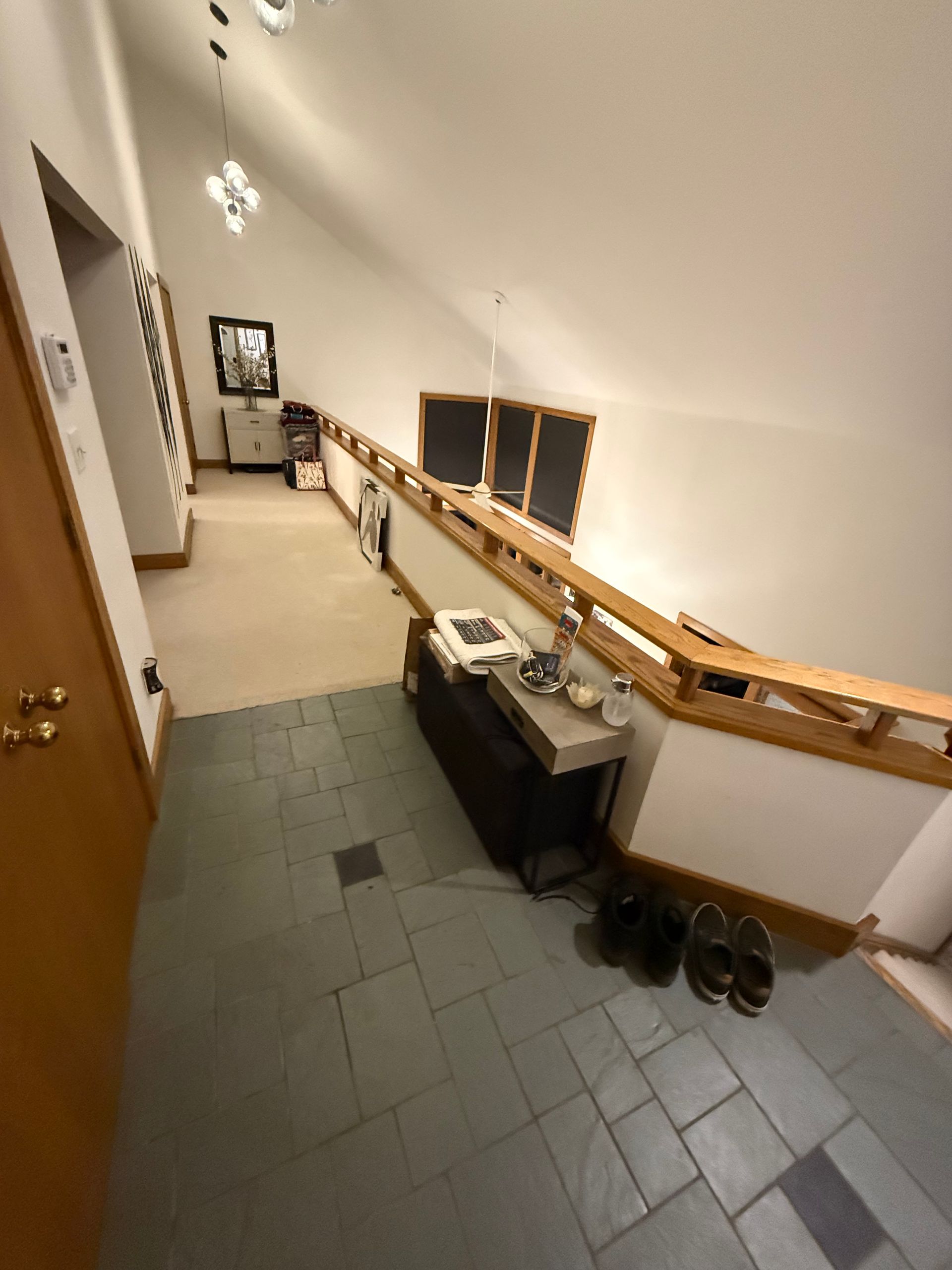 Narrow hallway with tiled floor, railing, sink, and two chalkboards under slanted white ceiling.