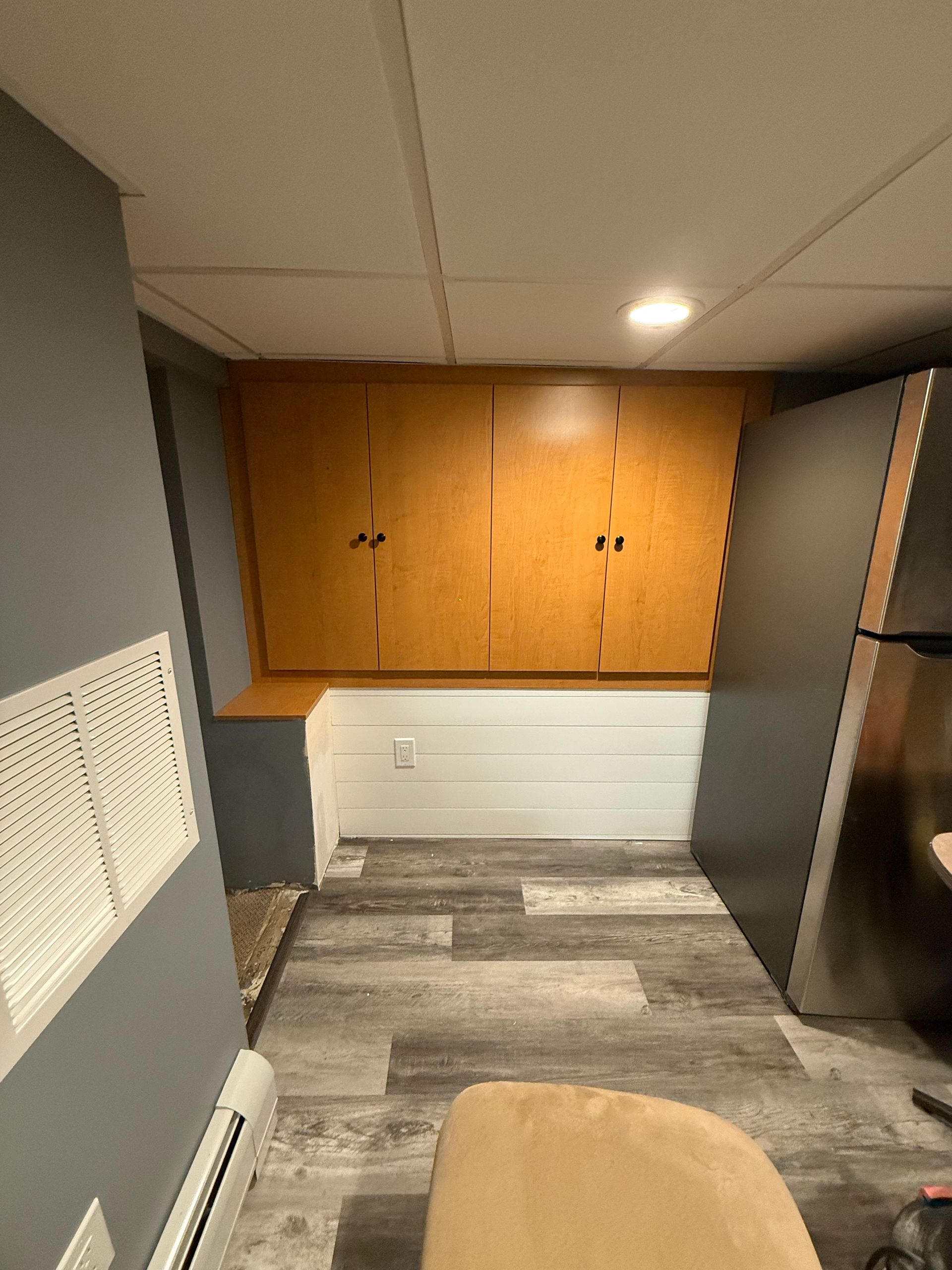 Small kitchen or office kitchenette with wooden cabinets, gray tile floor, and a stainless refrigerator.
