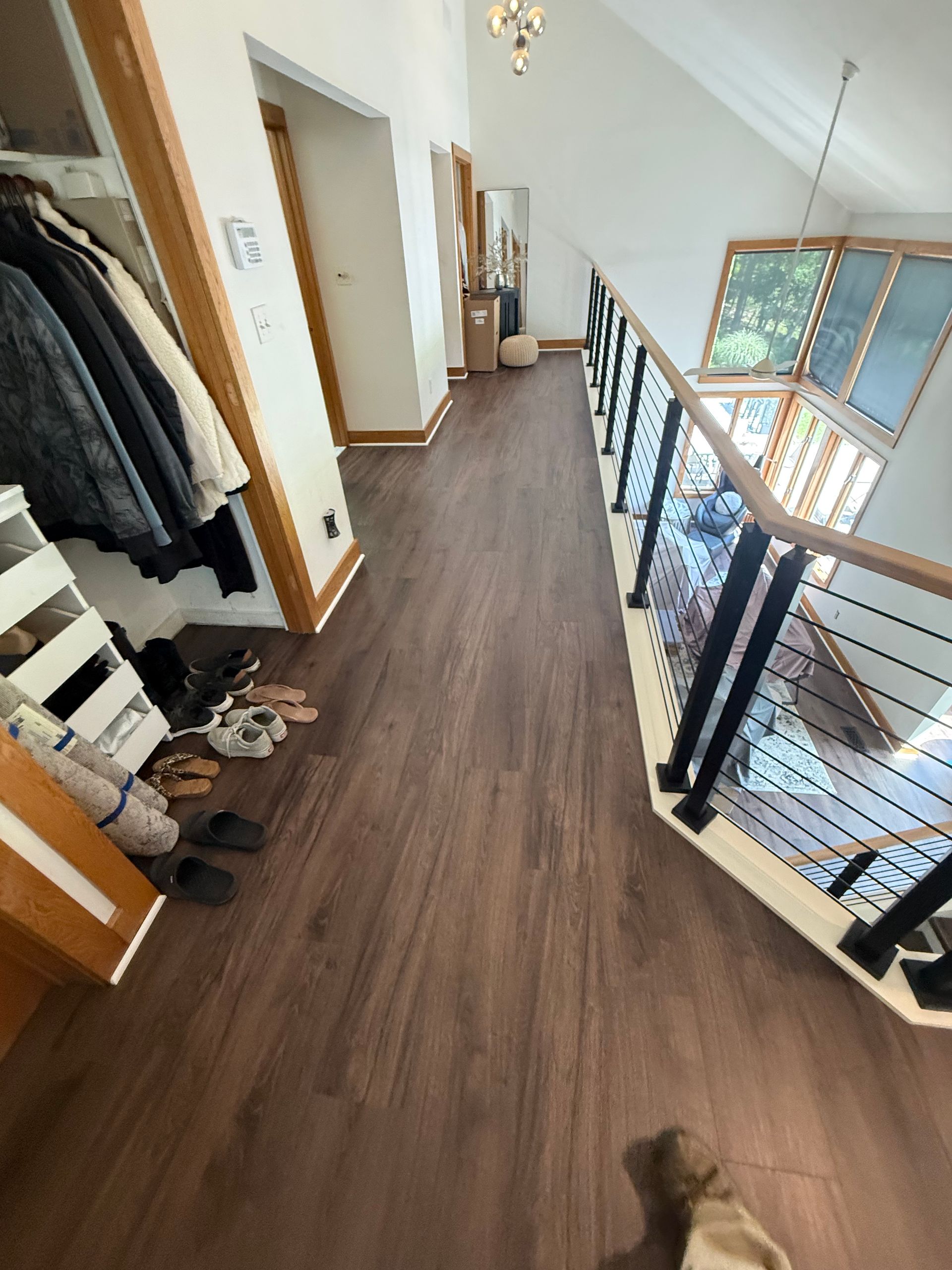 Hallway with wood flooring, railing, stairs, coat rack, and windows overlooking a lower level.