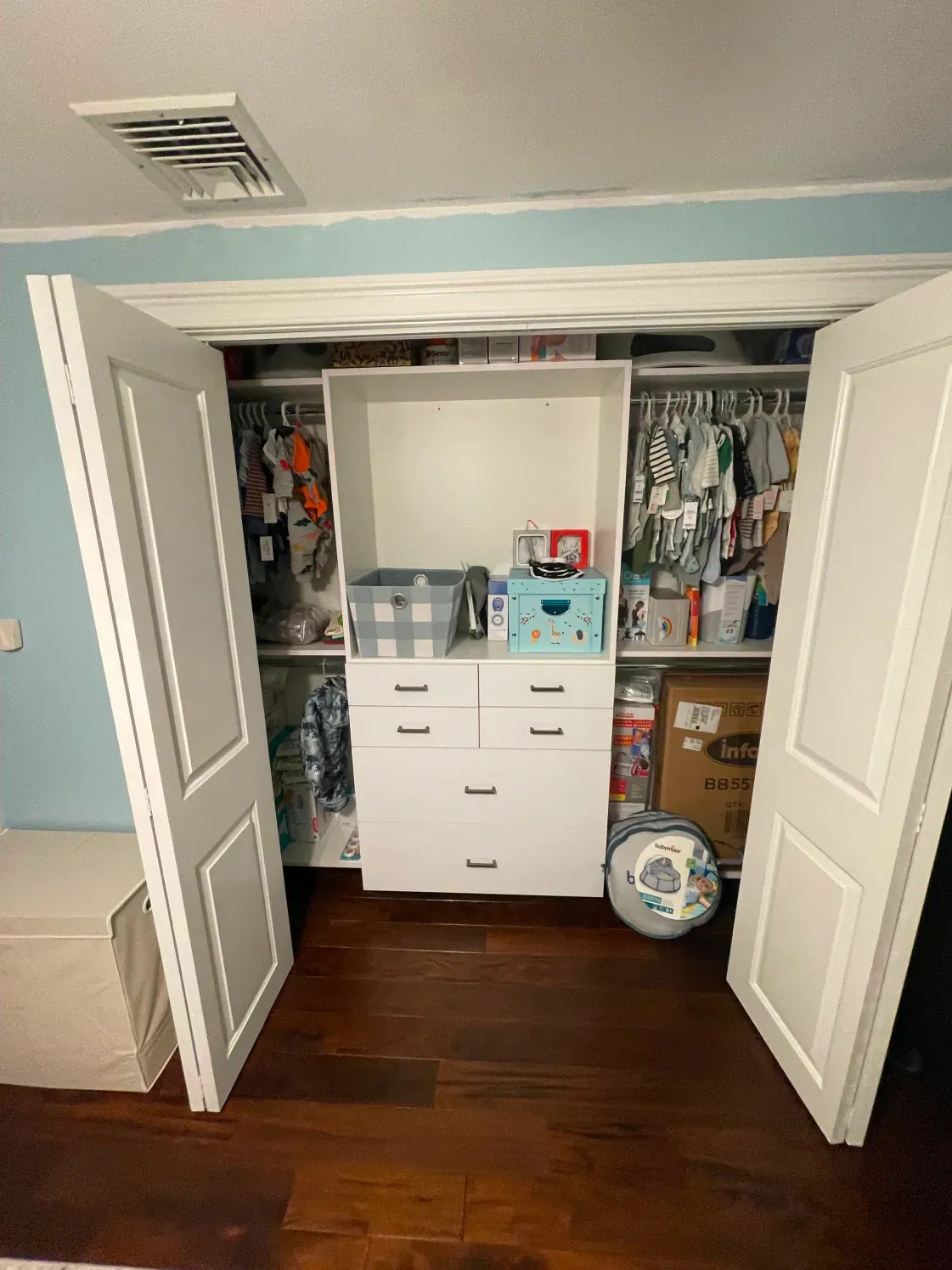 White closet with open doors, custom shelves, drawers, and baby clothes.
