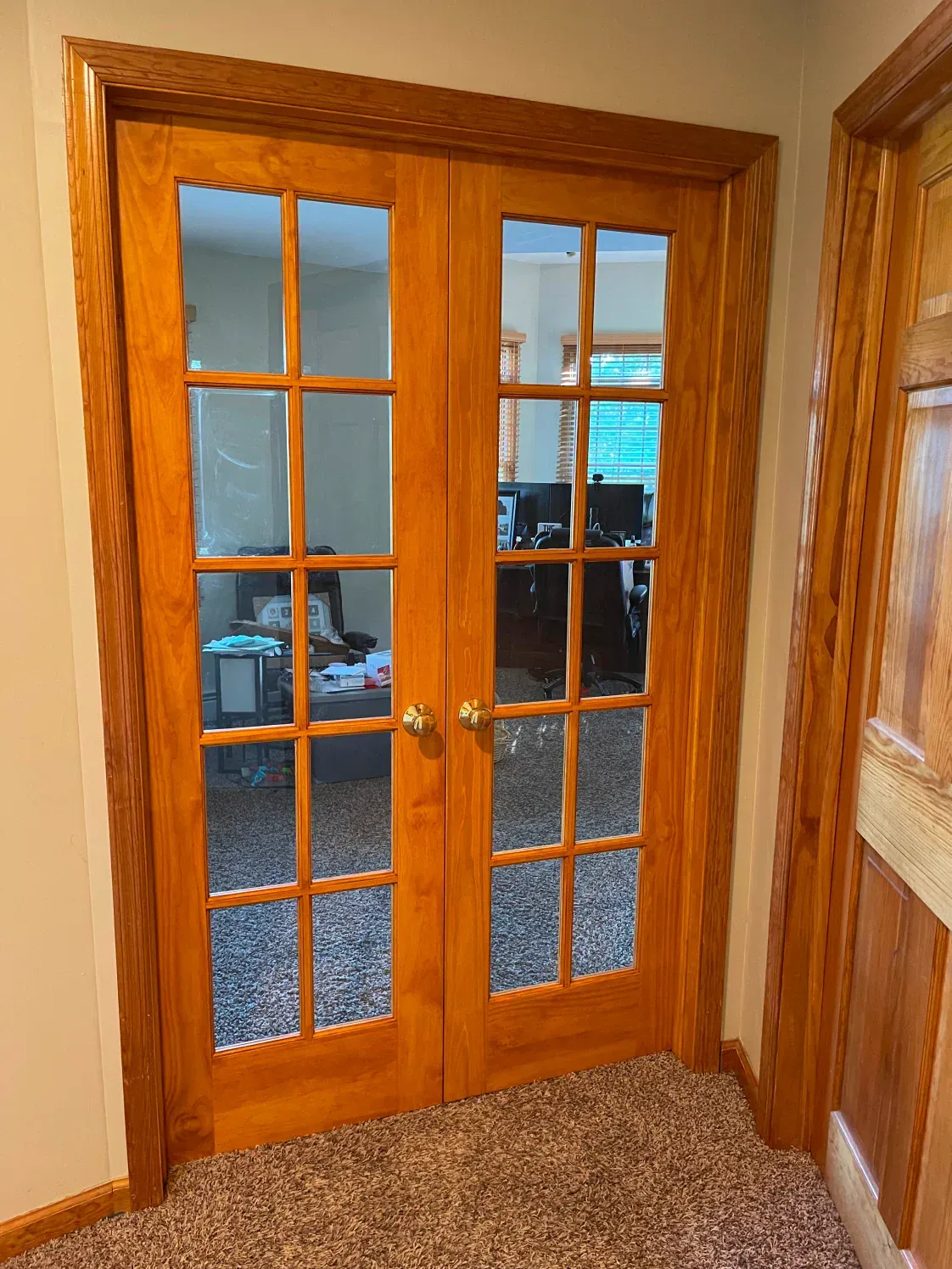 Wooden French doors with glass panes, set in a wood frame and trim, open to an office.