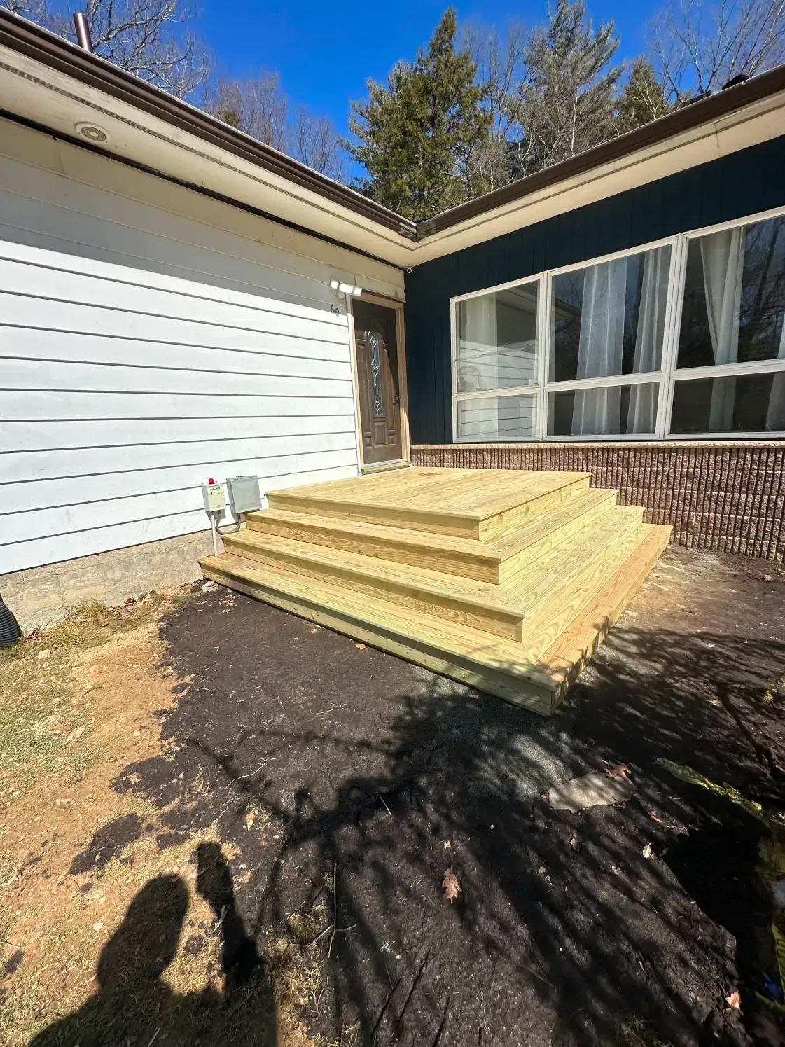 Newly constructed wooden steps leading to a house entrance. House has white siding and dark trim.