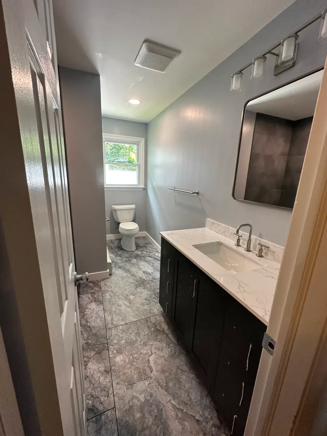 Bathroom with gray walls, dark wood vanity, patterned floor, and a toilet.