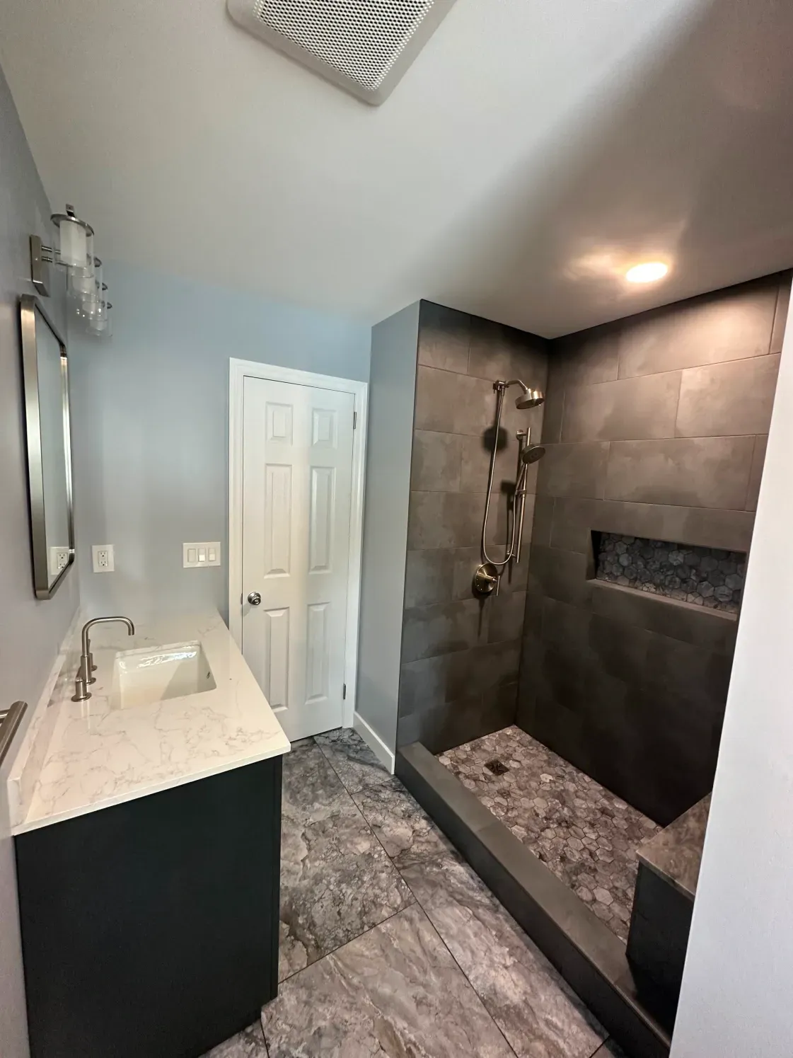 Modern bathroom with dark gray shower tile, vanity, and light blue walls.