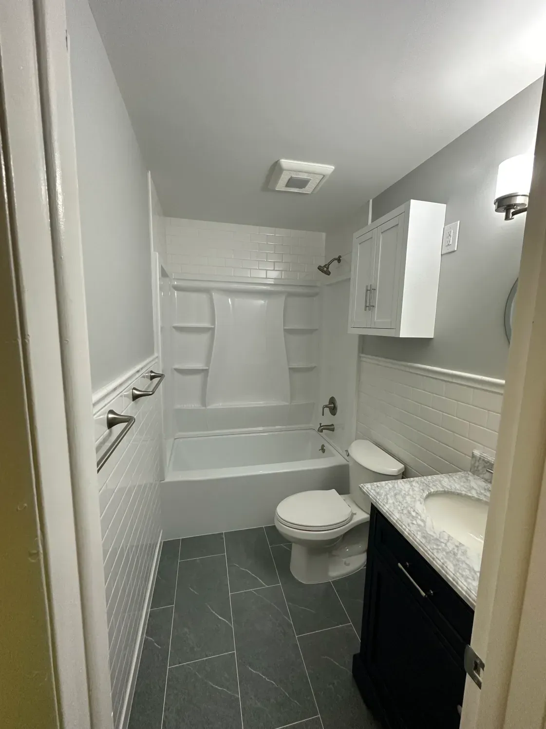 Bathroom with white tile, tub/shower, toilet, dark vanity, gray floor, and white walls.
