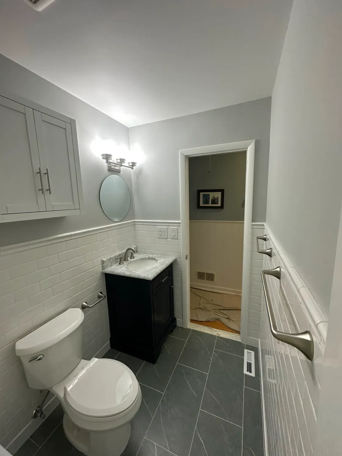 A newly remodeled bathroom with gray walls, a white tiled backsplash, and a black vanity.