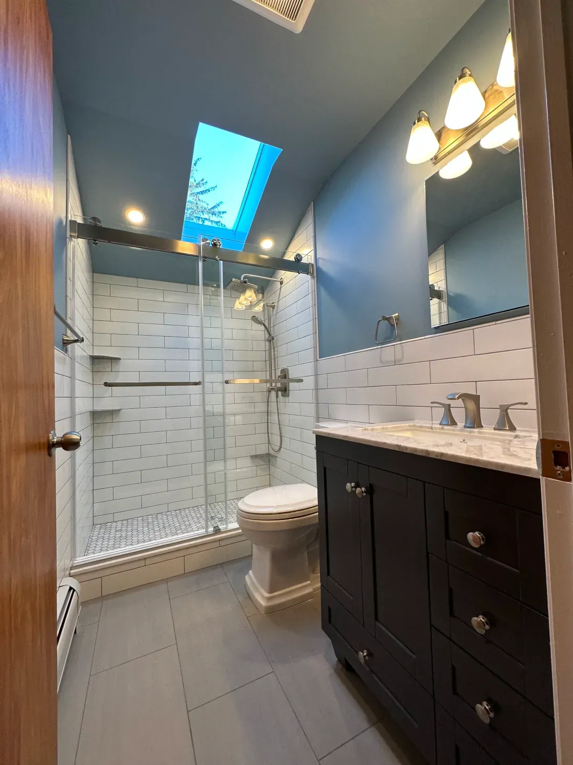 energy-efficient windows clermont Small bathroom with blue walls, skylight, shower, vanity, and toilet.