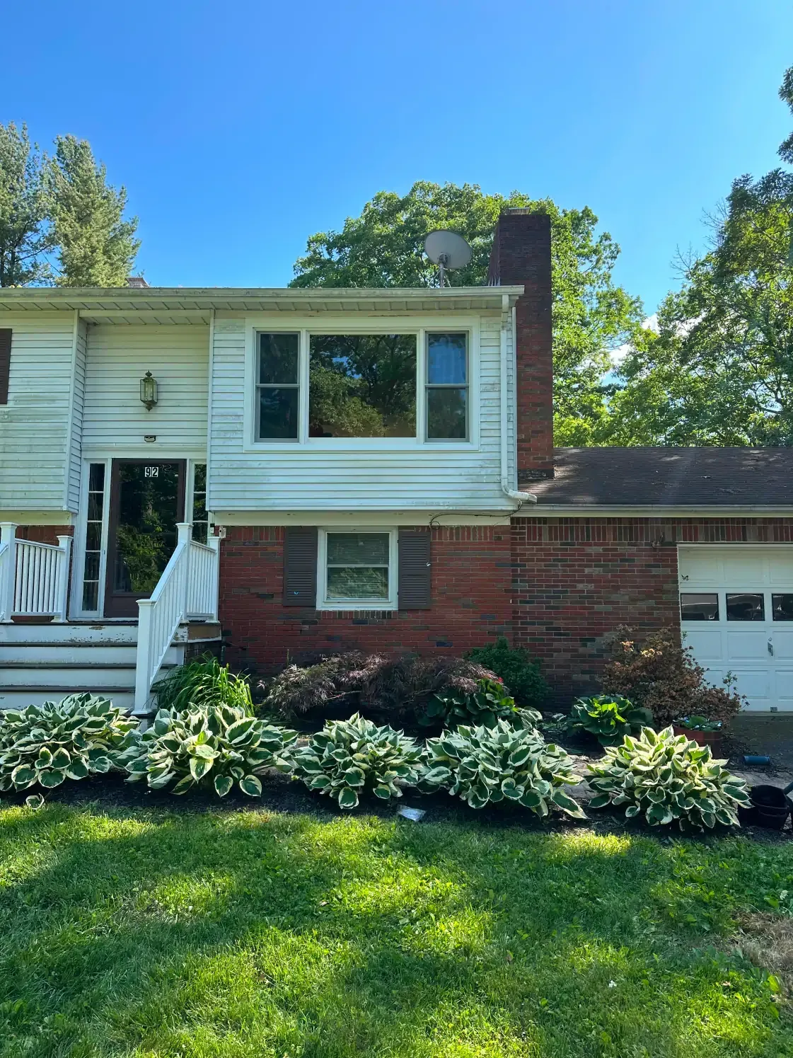 Split-level house with white siding, brick accents, and a garage, surrounded by landscaping on a sunny day.