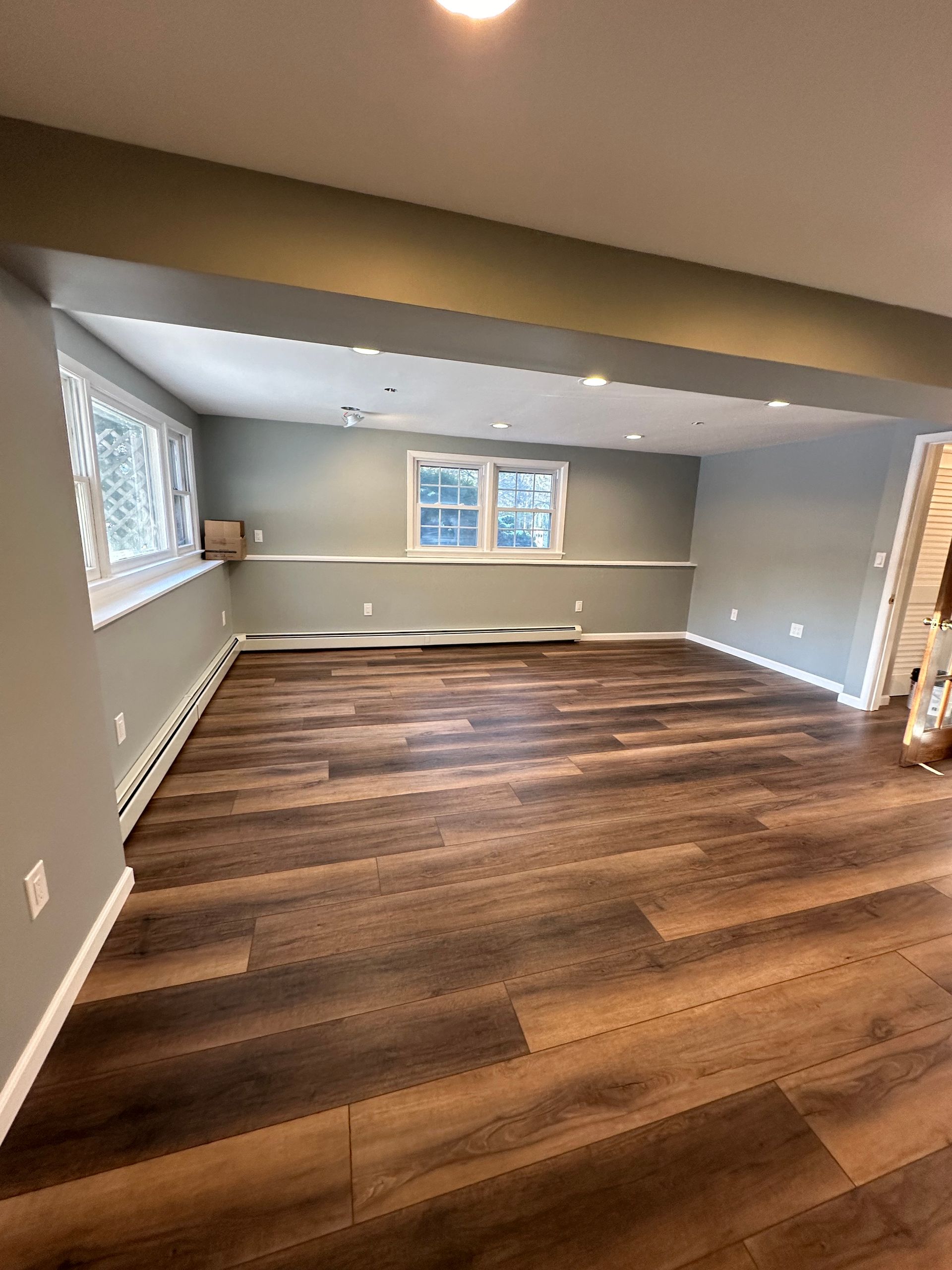 Empty living room with gray walls, wood floors, and windows along the far wall.