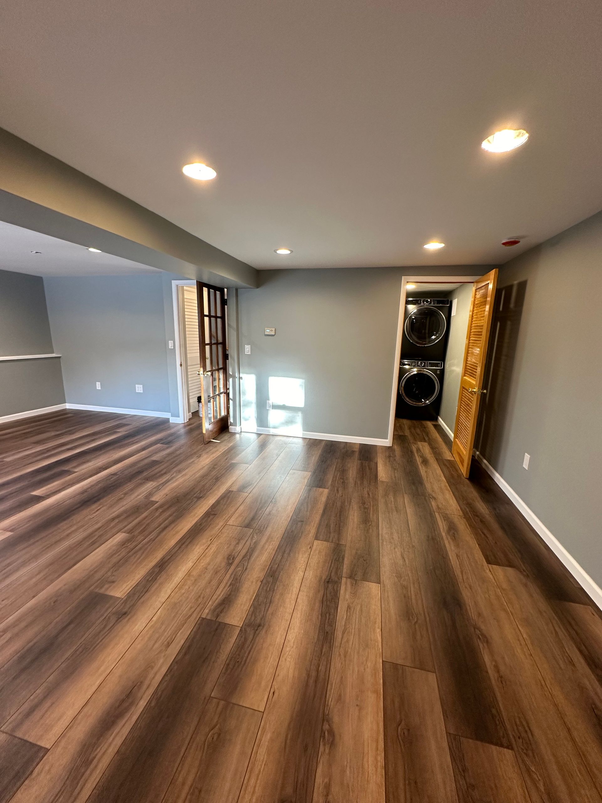 Empty modern room with wood floors, recessed lights, and a wall-mounted speaker stack near the back wall