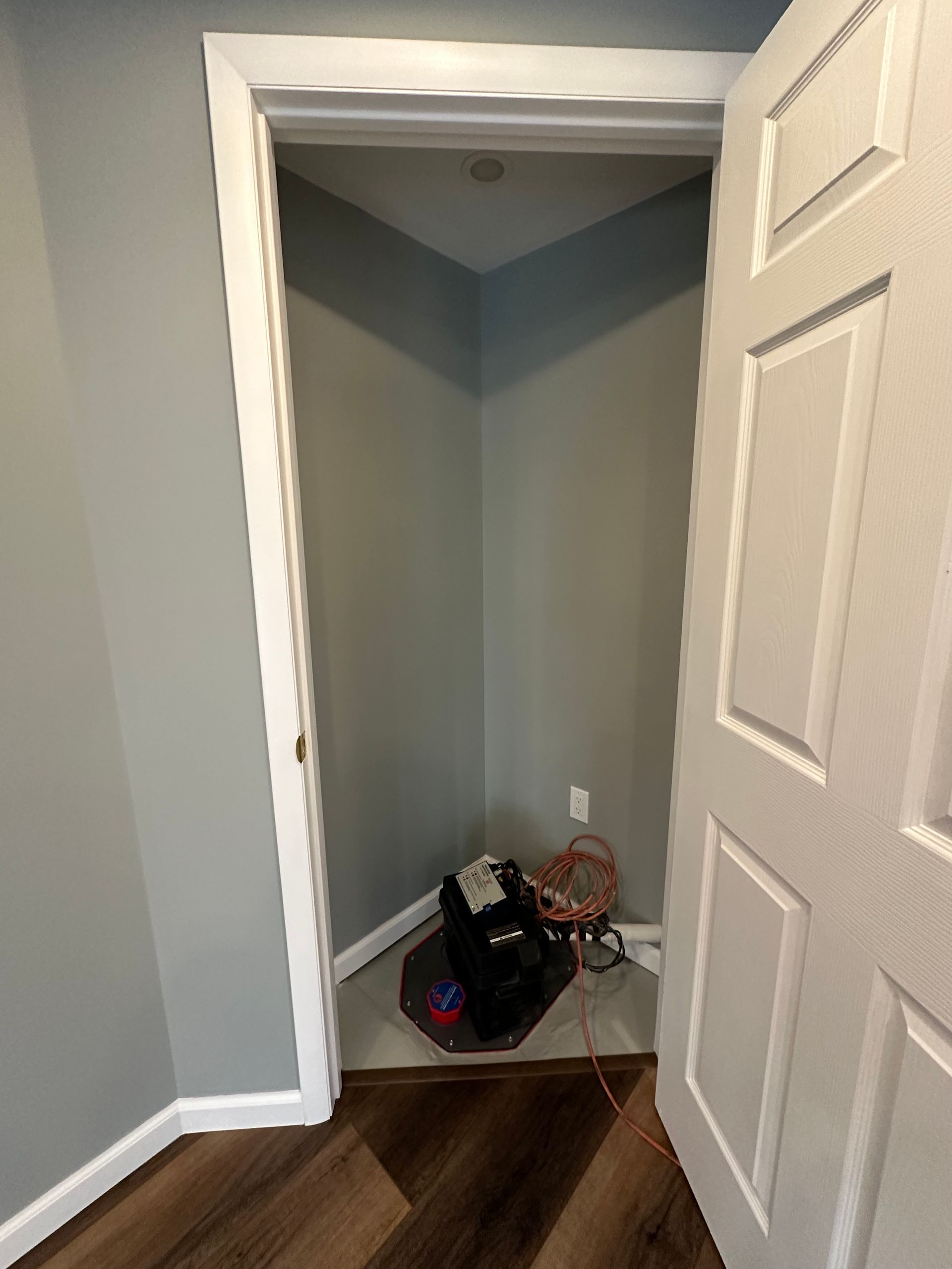 Open closet with gray walls, white trim, and a bag of cables on the floor near wood flooring.