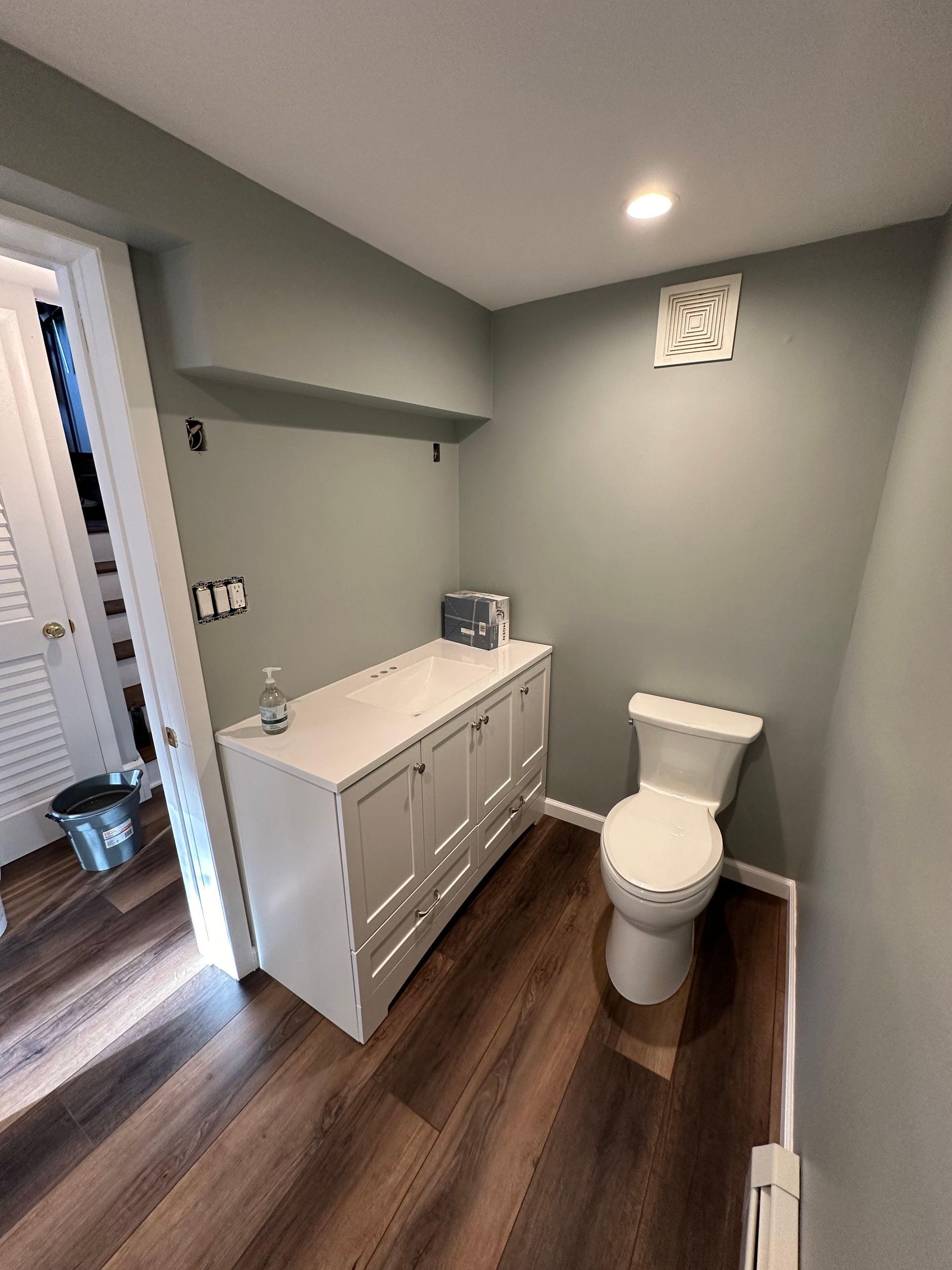 Modern bathroom with gray walls, white vanity, toilet, and wood-look flooring.