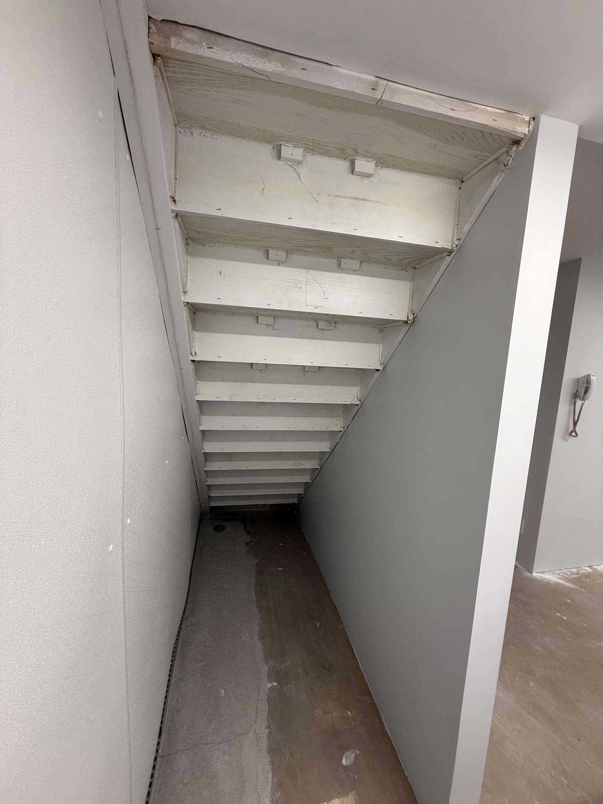 Narrow white stairwell with steep steps leading down into a dim corridor