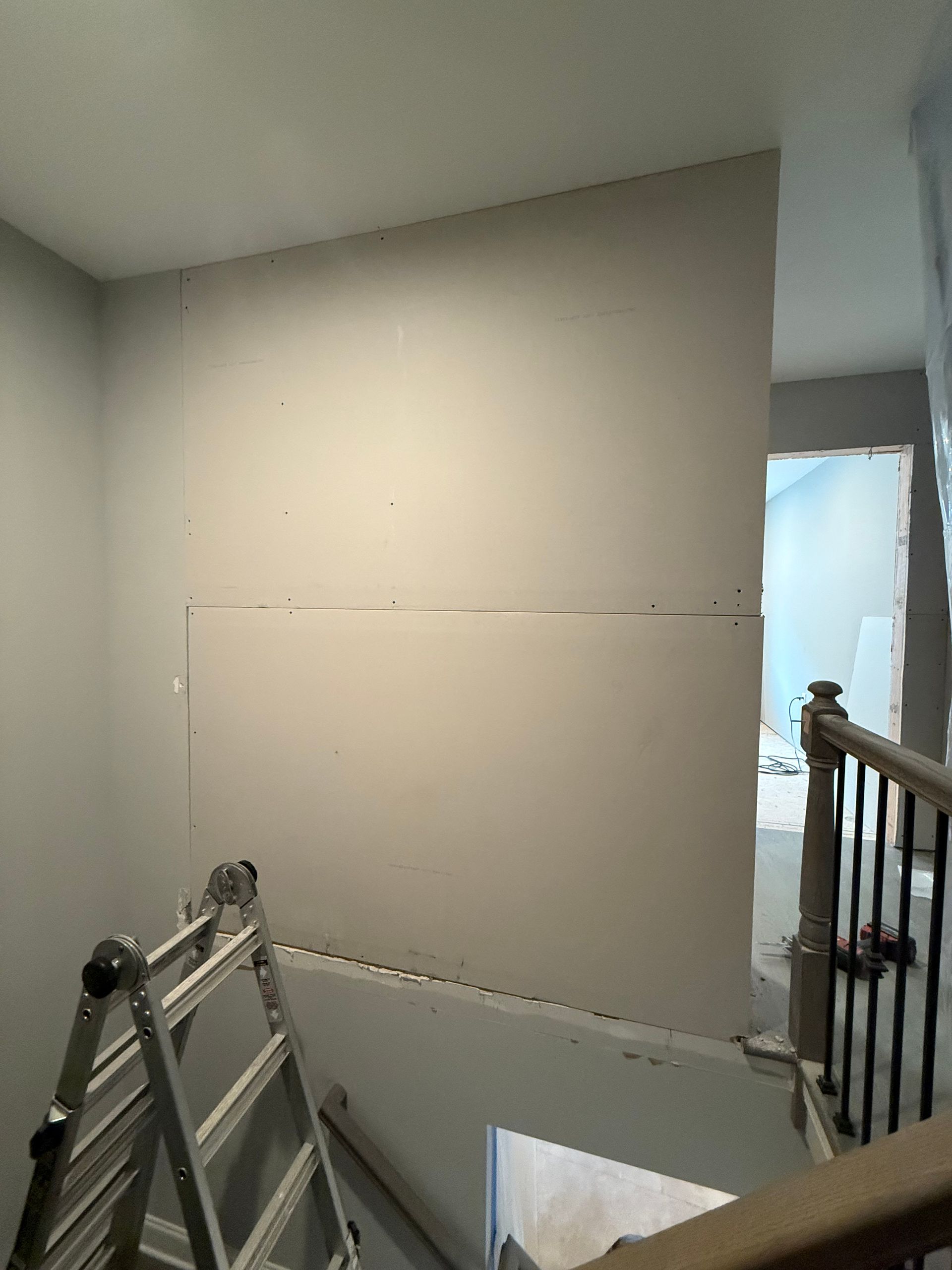 Stairwell with beige walls, a leaning ladder, and a railing beside a bright window.