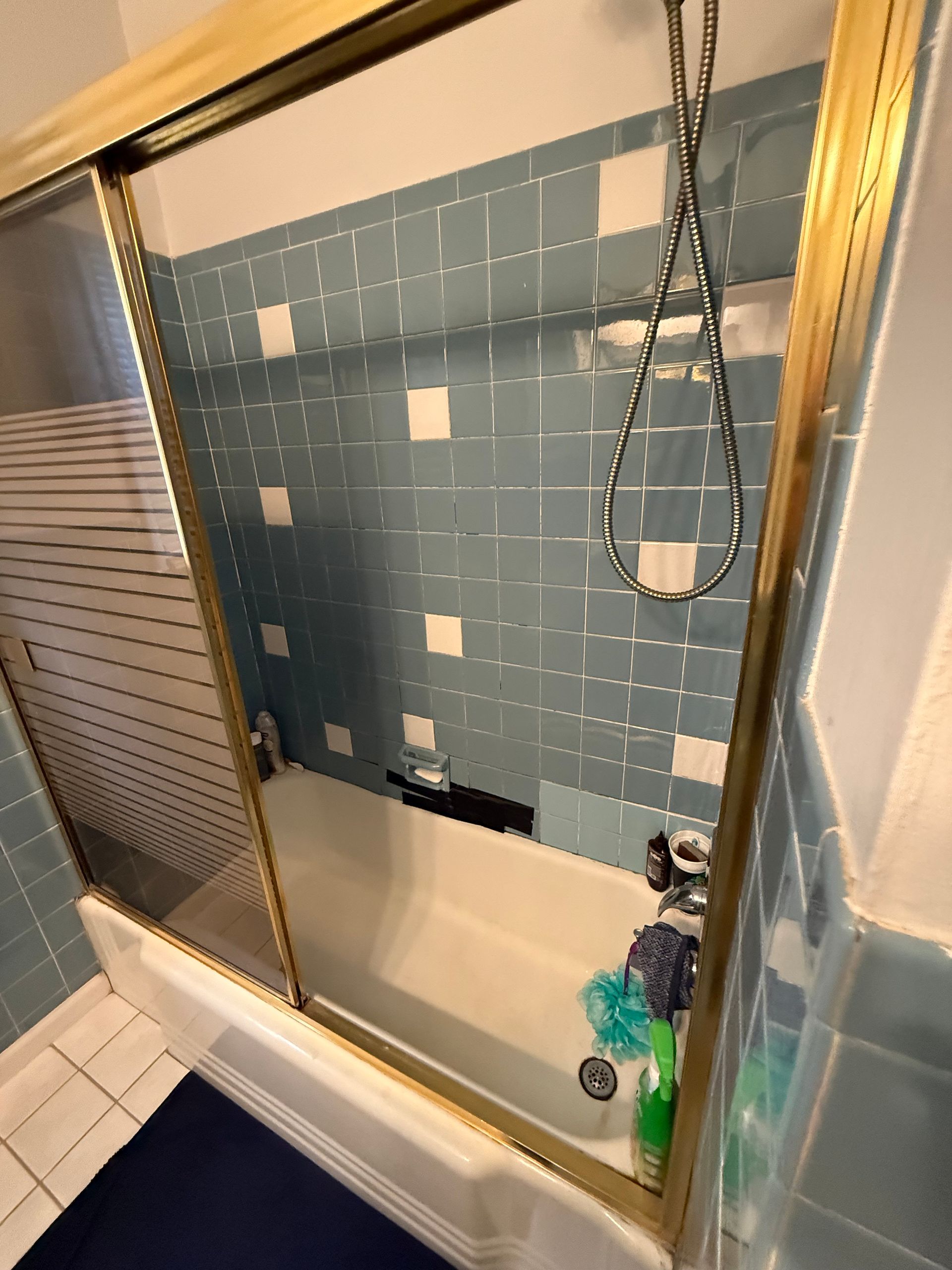 Partially tiled shower wall with blue tiles, missing sections, and a hanging shower head hose