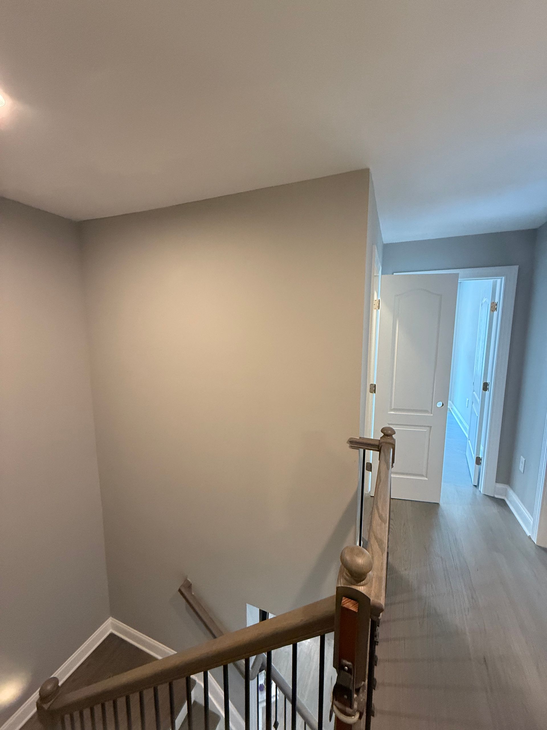 Interior hallway with stairs, gray walls, wood floor, and white doors leading to a bright room