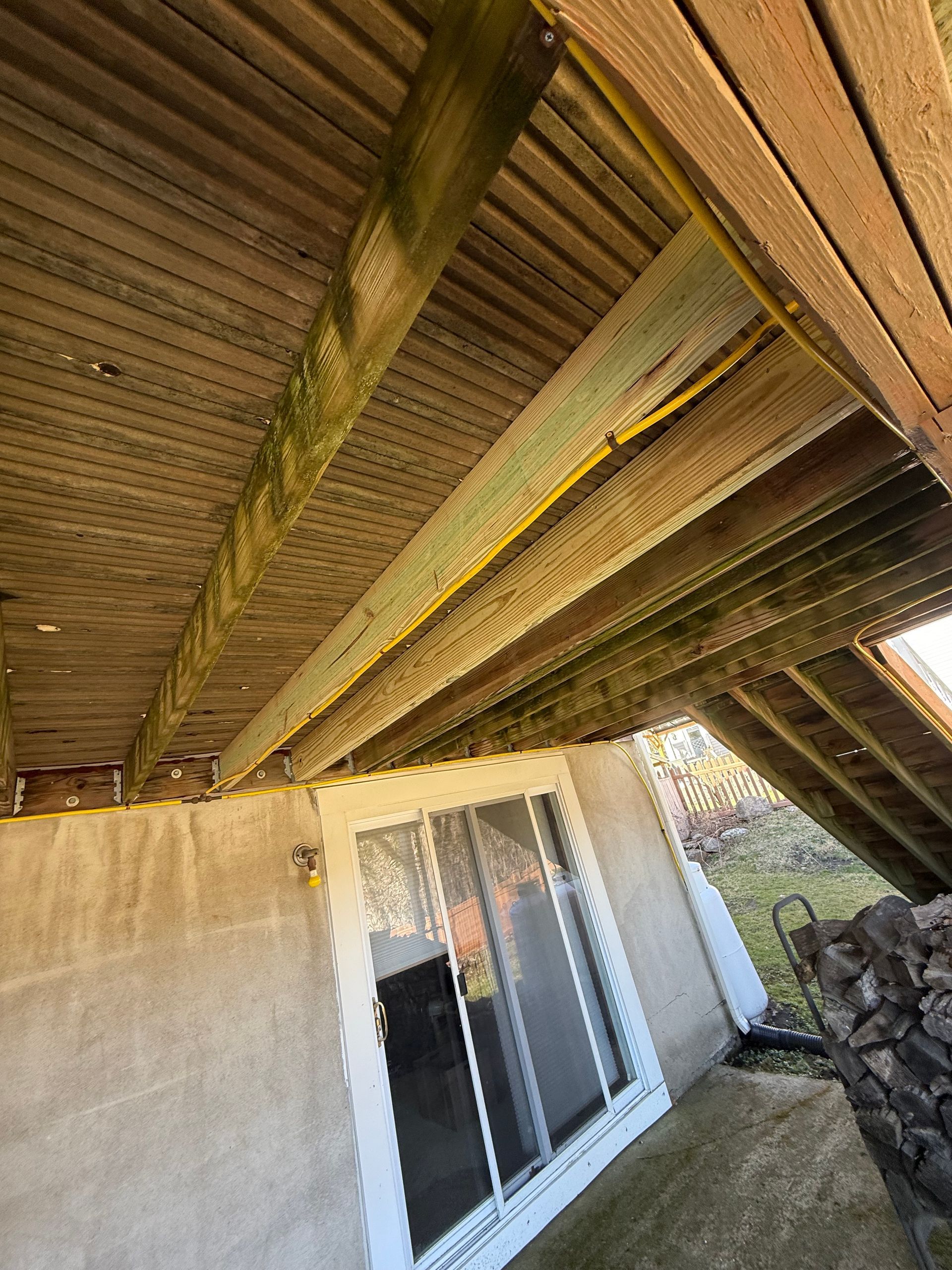 Underneath of a wooden deck. Deck beams show algae. House wall and sliding glass door are visible below.