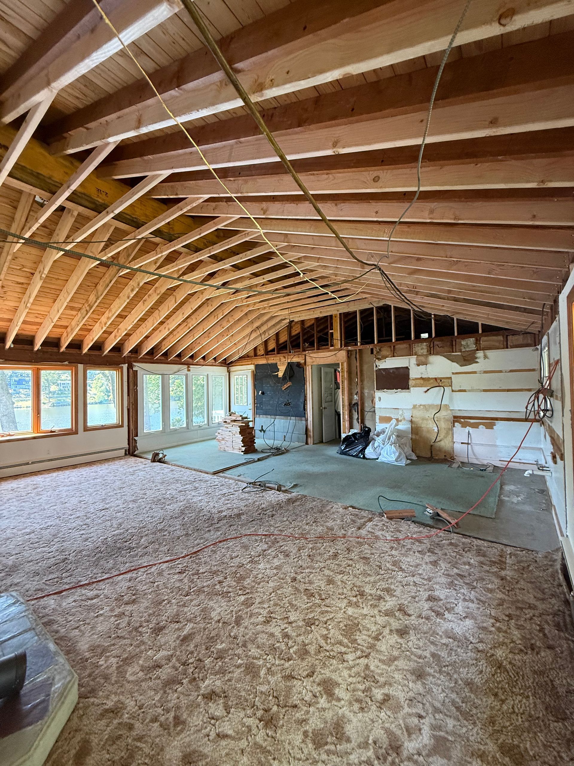 Interior of a home under renovation, showing exposed wooden beams, old flooring, and drywall removed.