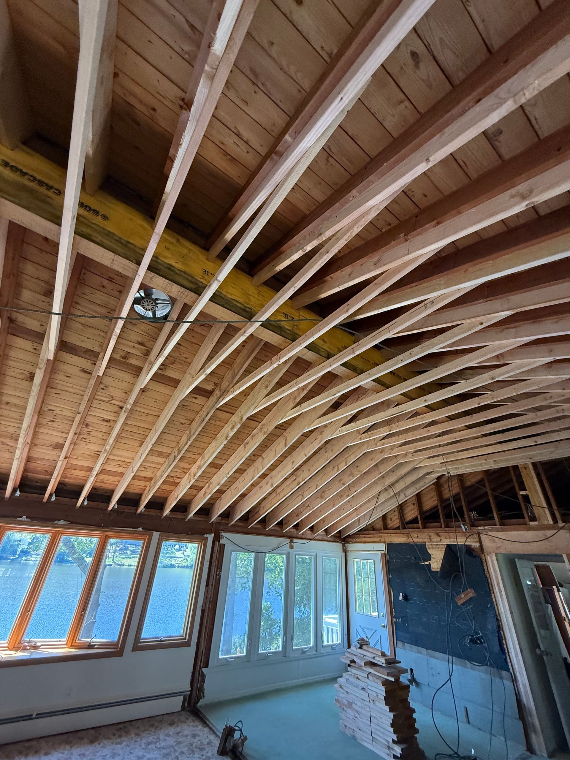 Interior construction site; exposed rafters and beams in a room with windows and partially demolished walls.