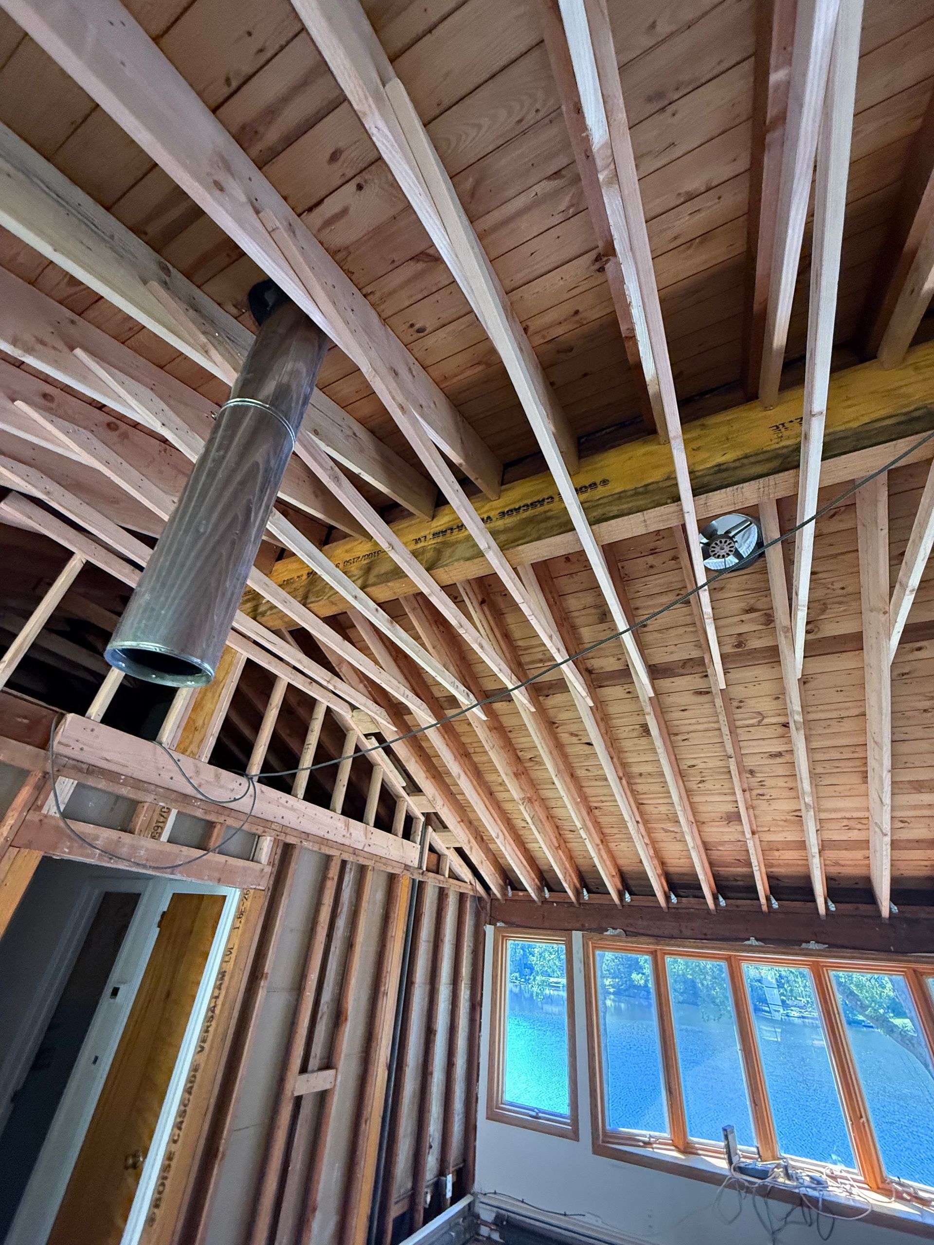 Interior view of a building under construction, showing wooden framing, exposed beams, and a metal chimney.