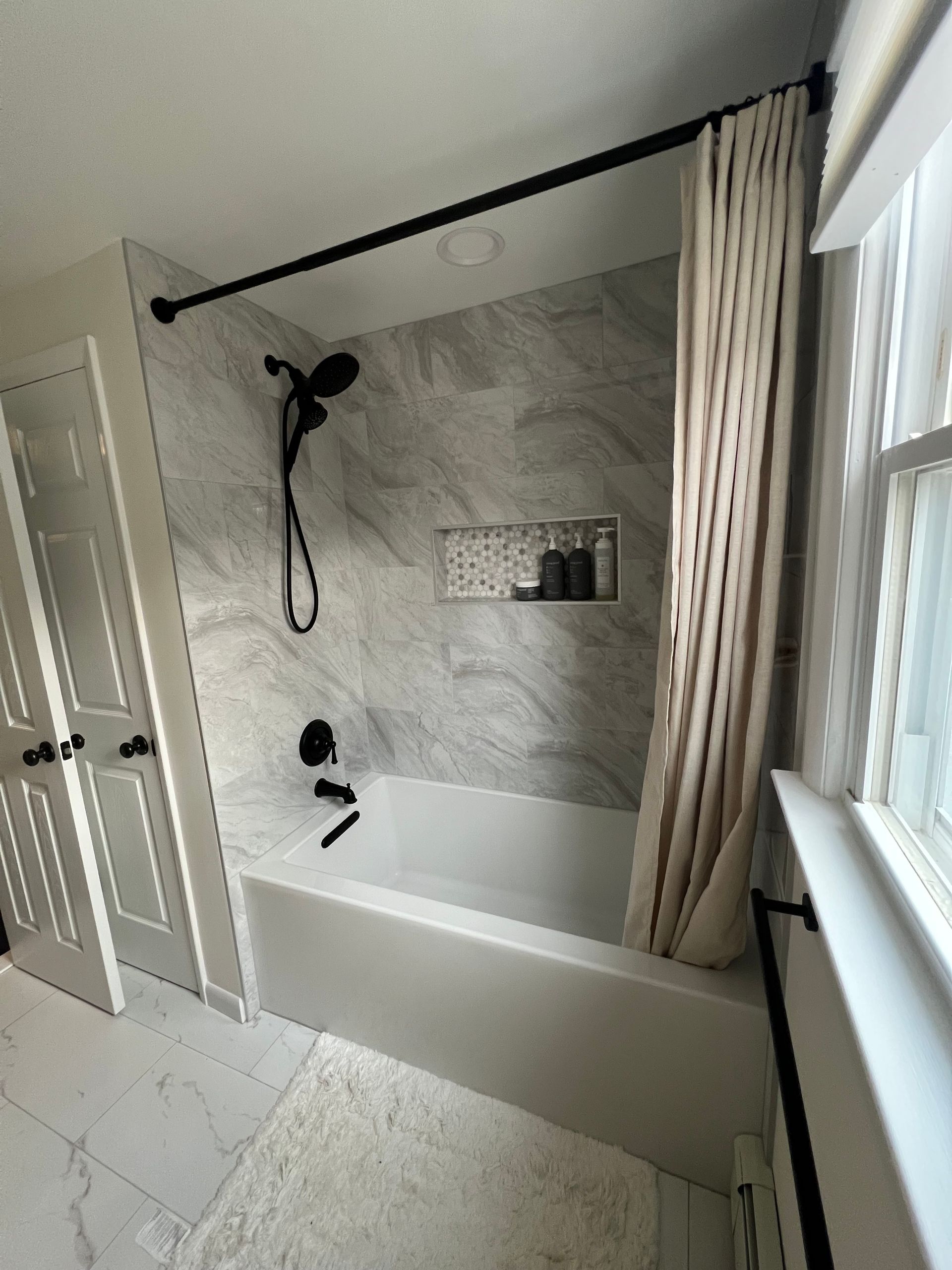 Bathroom with white tile, a bathtub, black shower fixtures, and a neutral curtain.