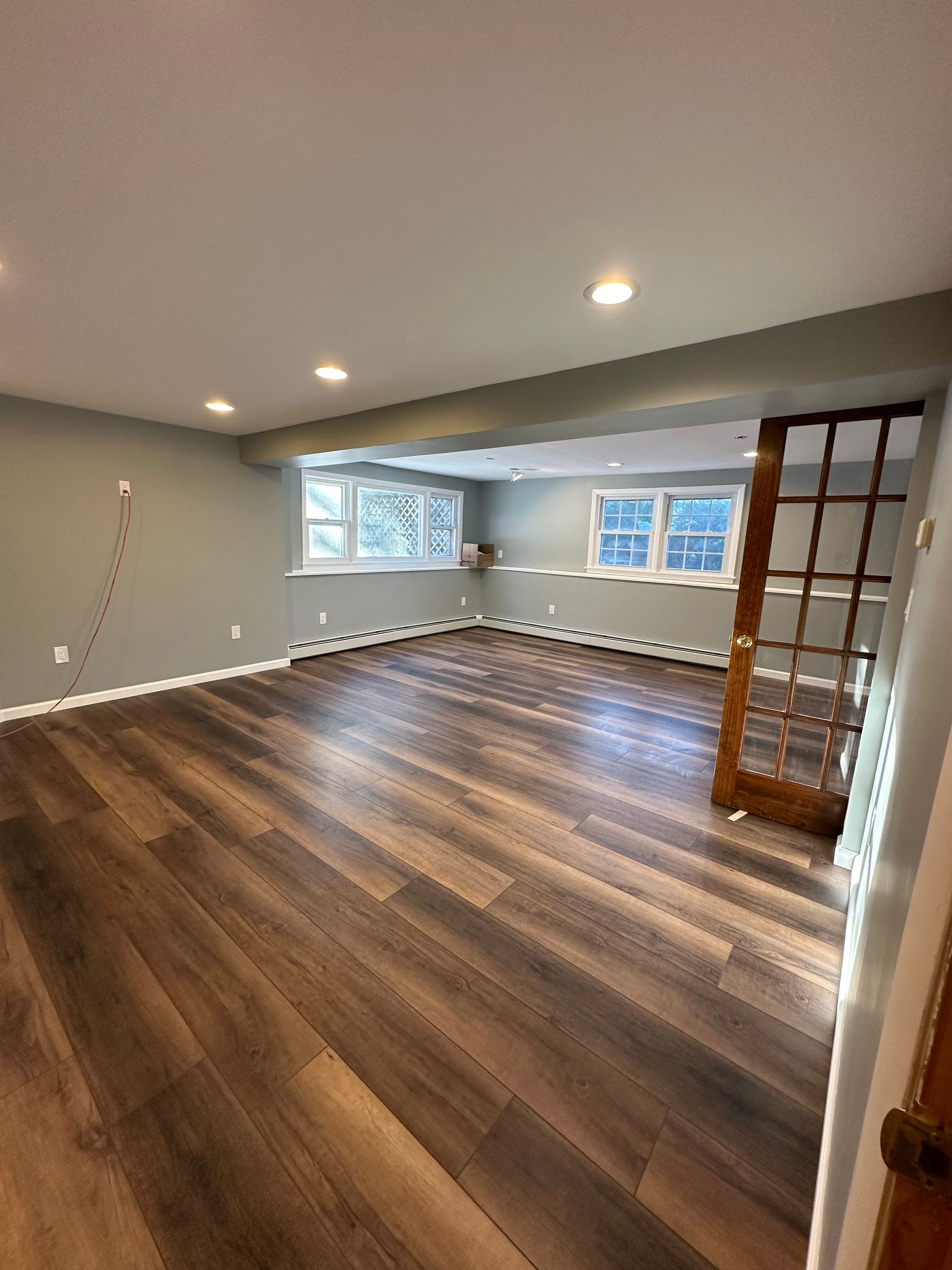 Empty room with hardwood floors, light green walls, and three windows. A brown door stands open.