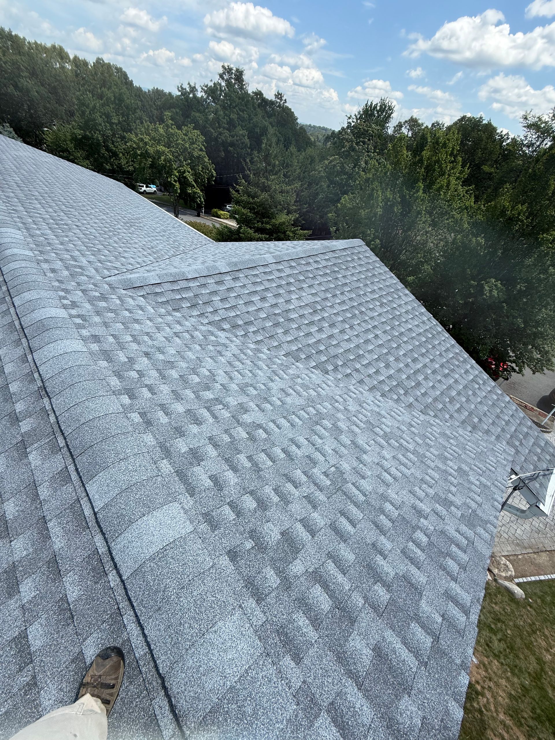 View of a recently shingled roof with trees in the background under a blue sky.