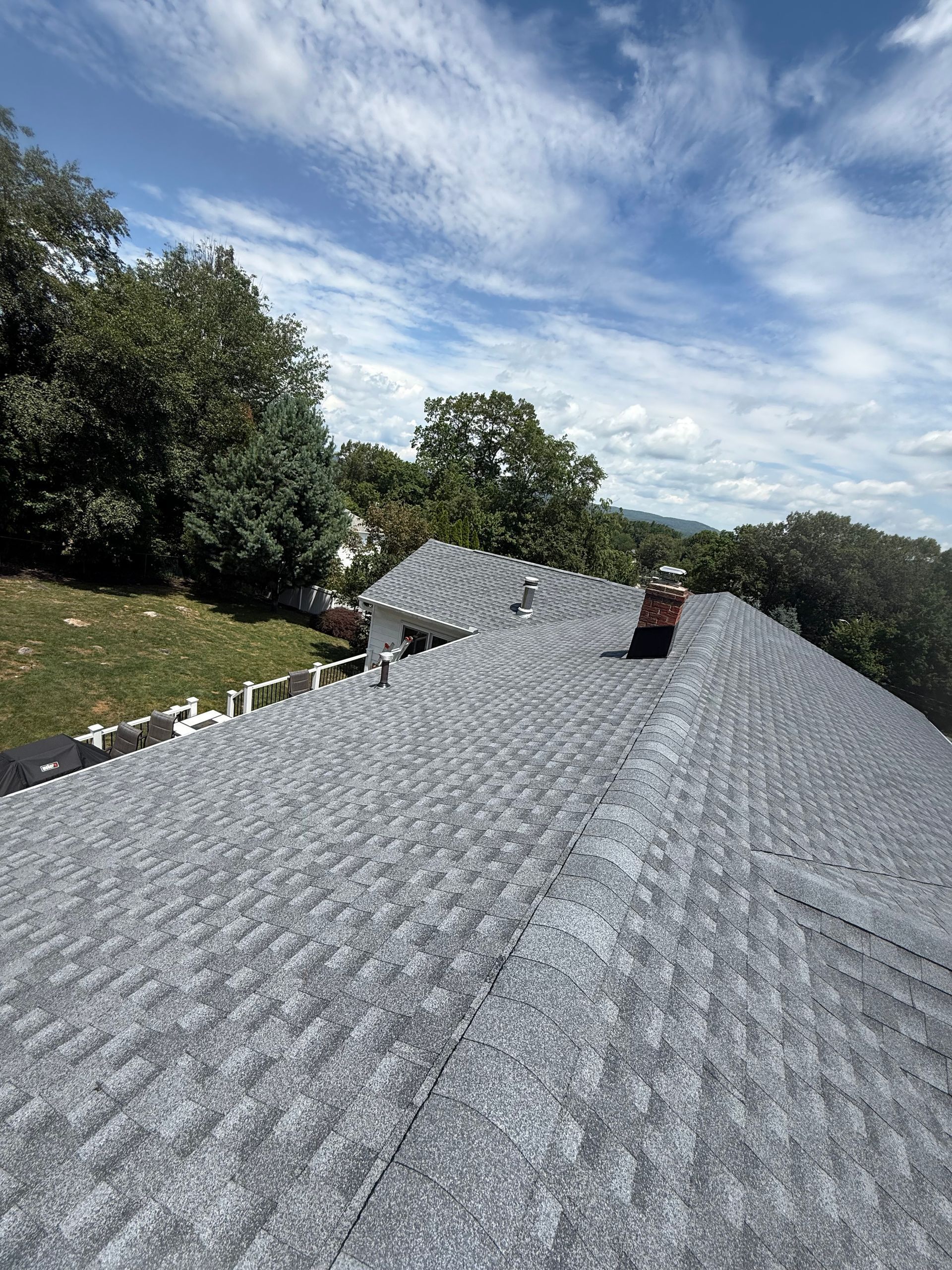 Workers installing gray shingles on a rooftop on a sunny day.