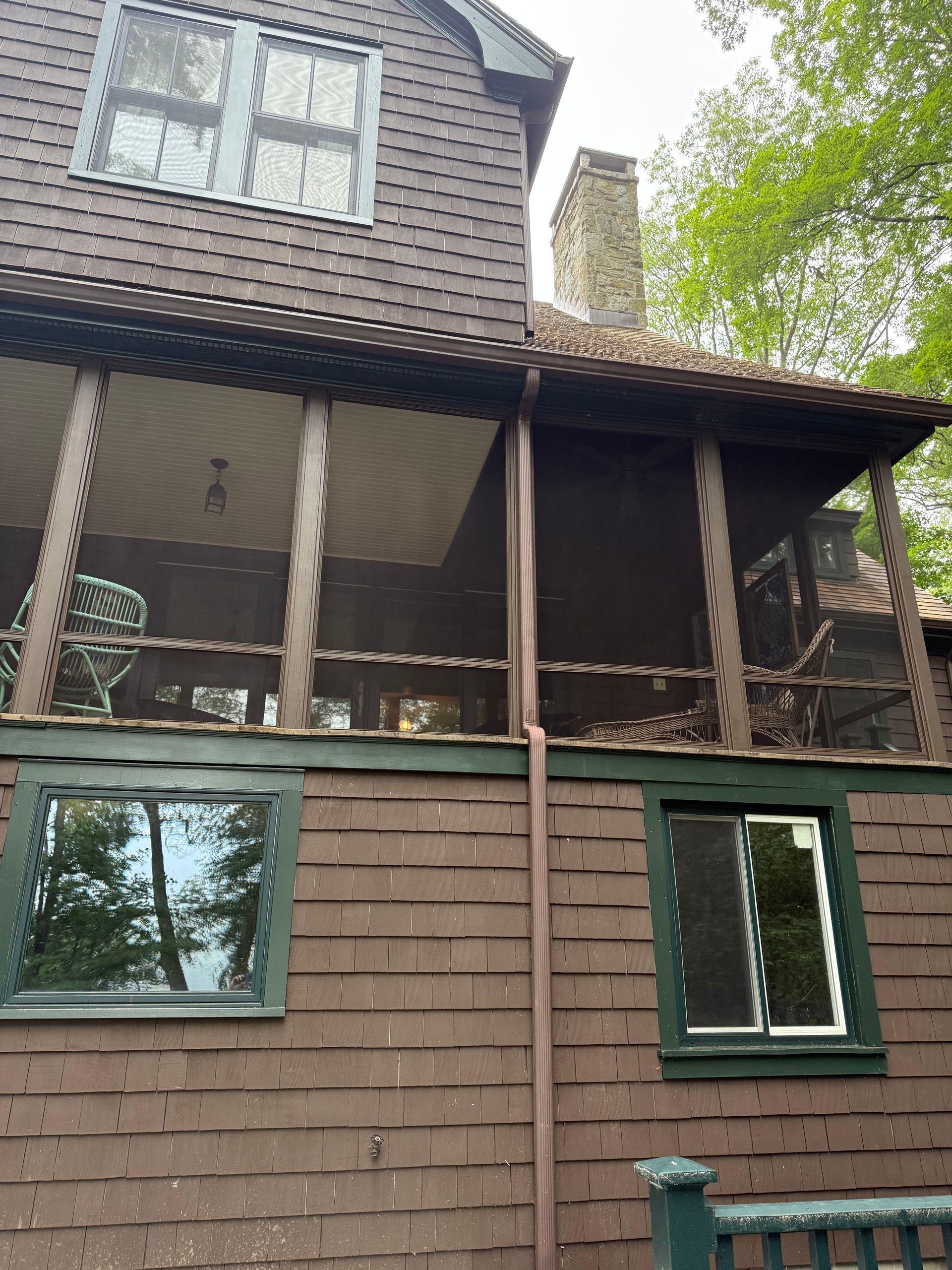 Brown shingled house with a screened porch and windows; a chimney is visible.