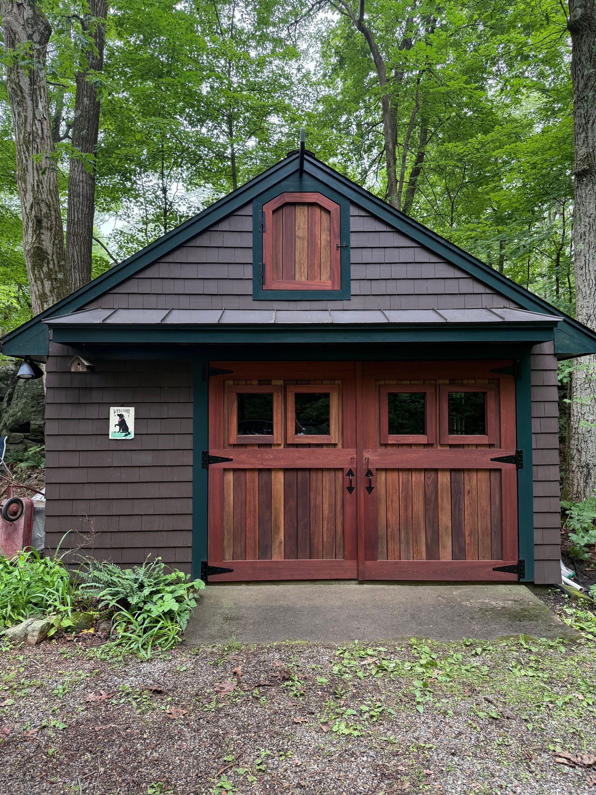 Brown shed with red double doors, small window above. Green trim, surrounded by trees.