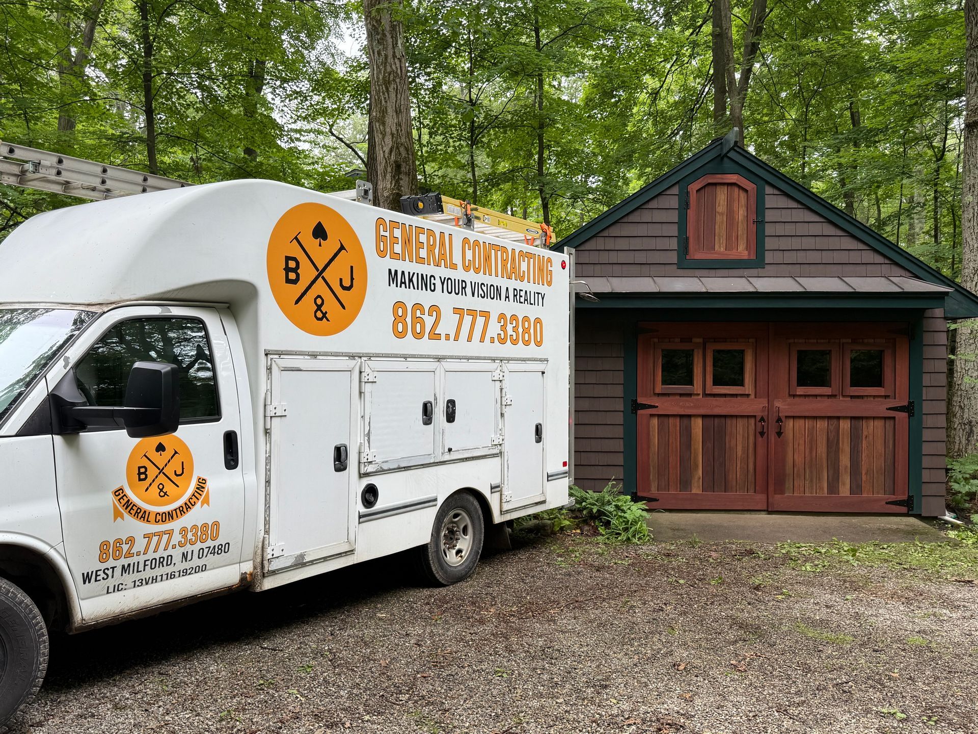 White work van parked next to a small wooden garage. The van has a company logo and phone number.