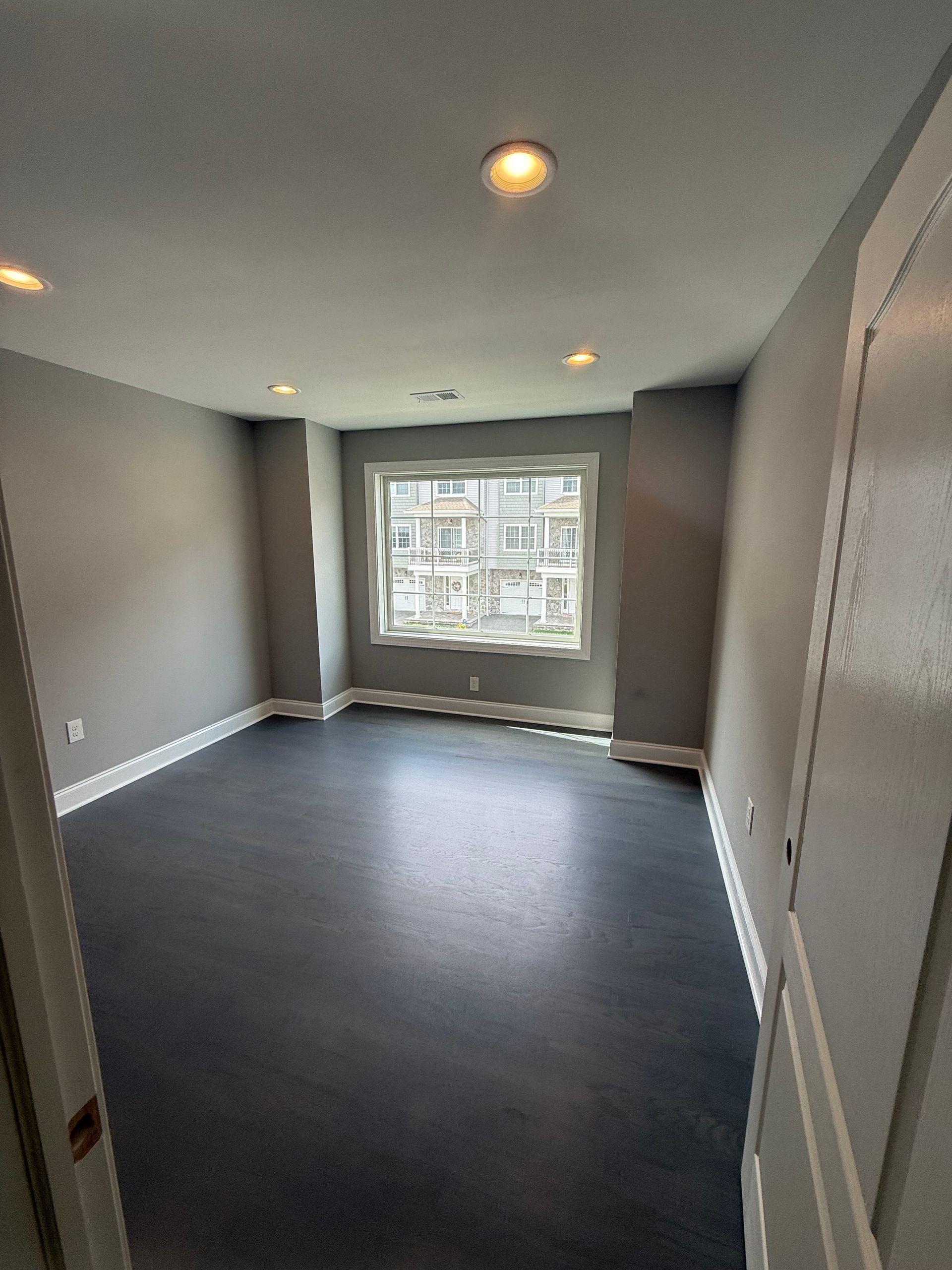 Empty room with gray walls, dark floor, and a window.
