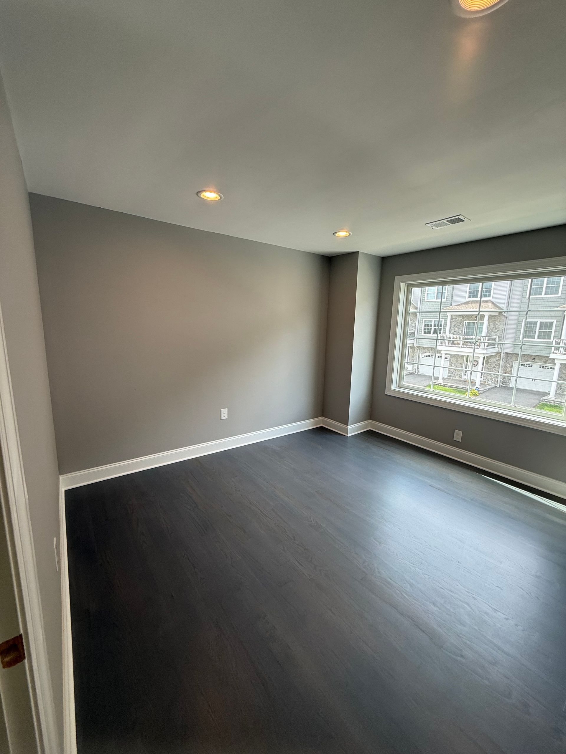 Empty room with dark wood floor, gray walls, white trim, and a window.