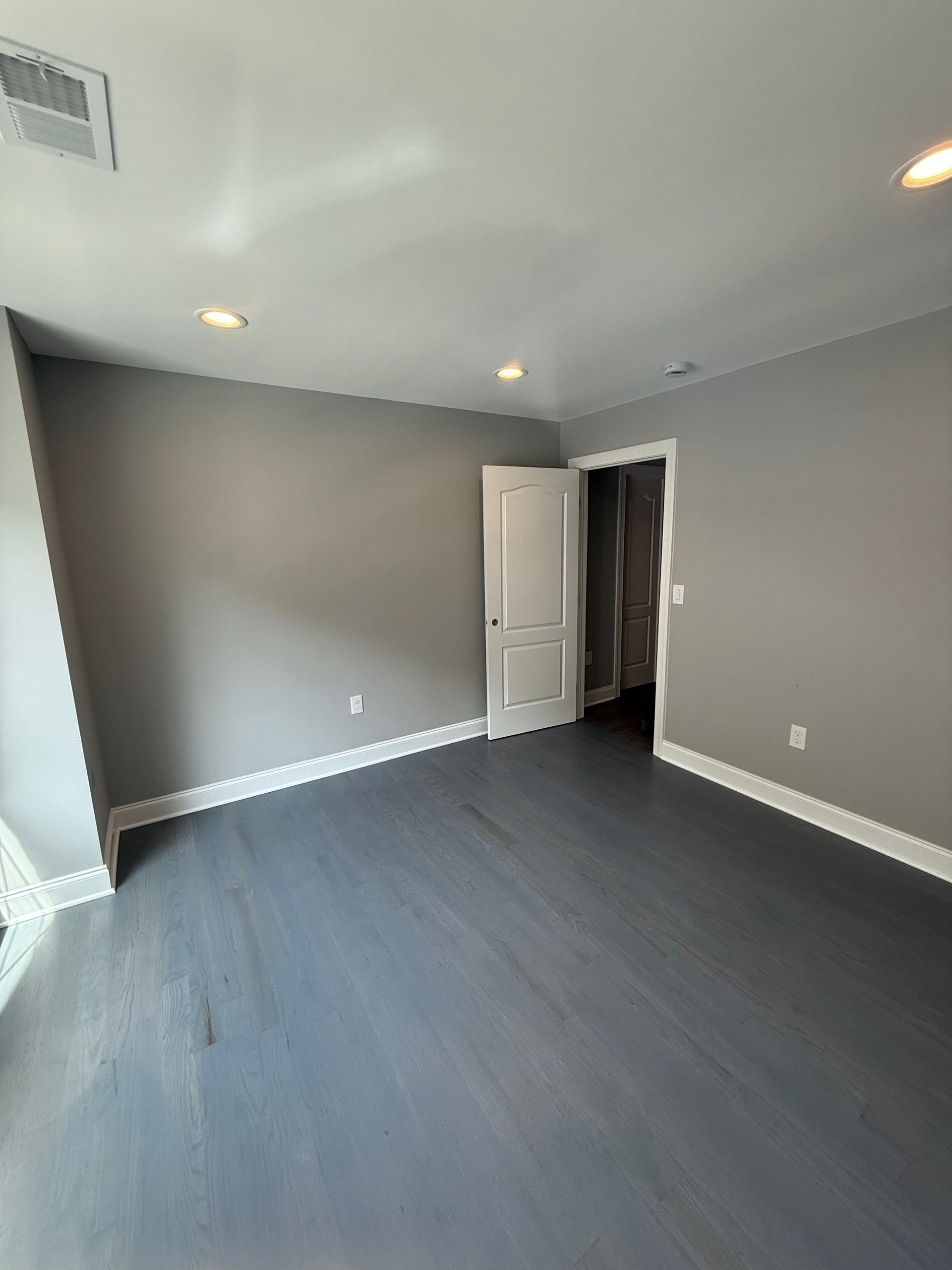 Empty room with gray walls and dark gray wood floor, white trim, and a white door.