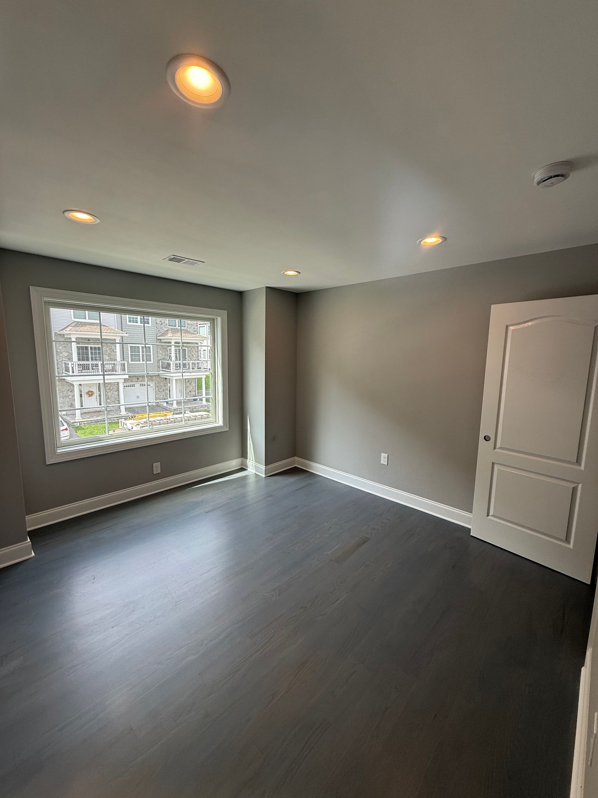 Empty room with gray walls, dark wood floor, and a window with a view of buildings.